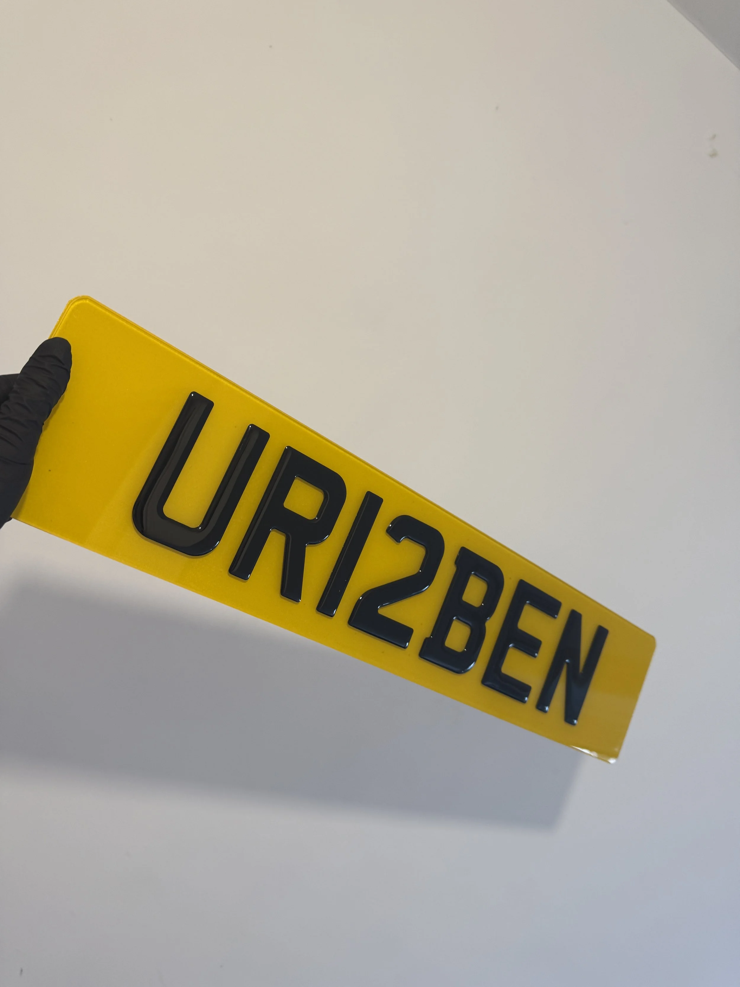 Hand wearing a black glove holding a yellow service sign with black raised lettering that reads 'URI/28BEN'.