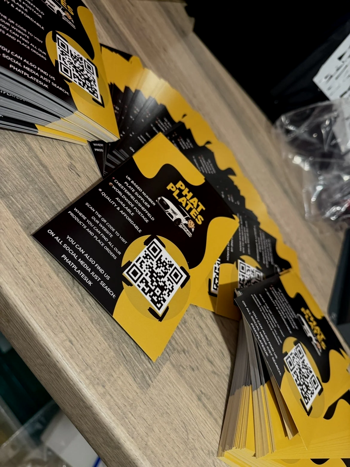 Several yellow and black flyers for PHAT PLATES UK with QR codes and contact information, laid out on a wooden surface.
