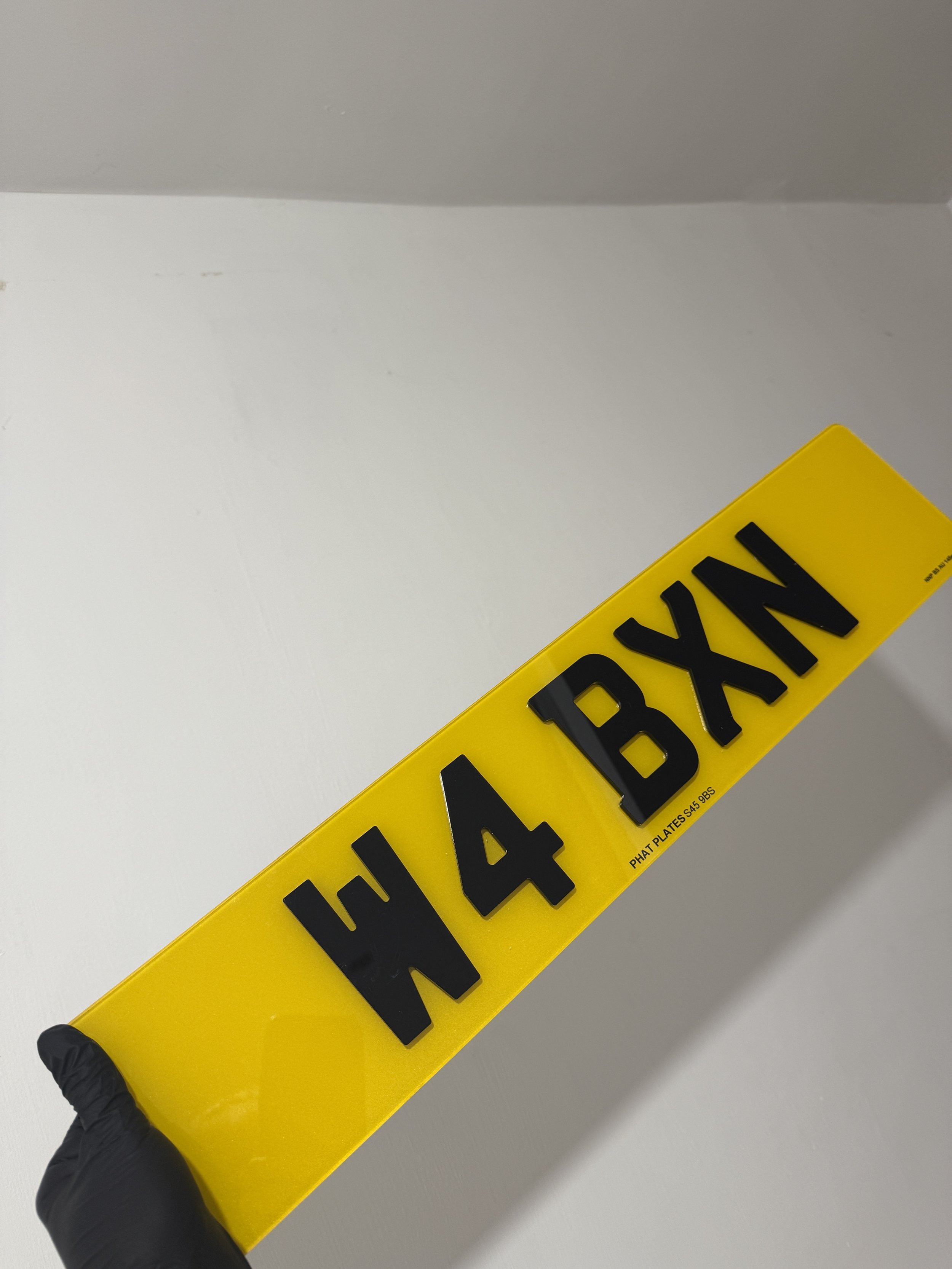 Yellow tag with black embossed letters 'H 4 BXXN' and small text 'PHAT PLATES S4 985'.