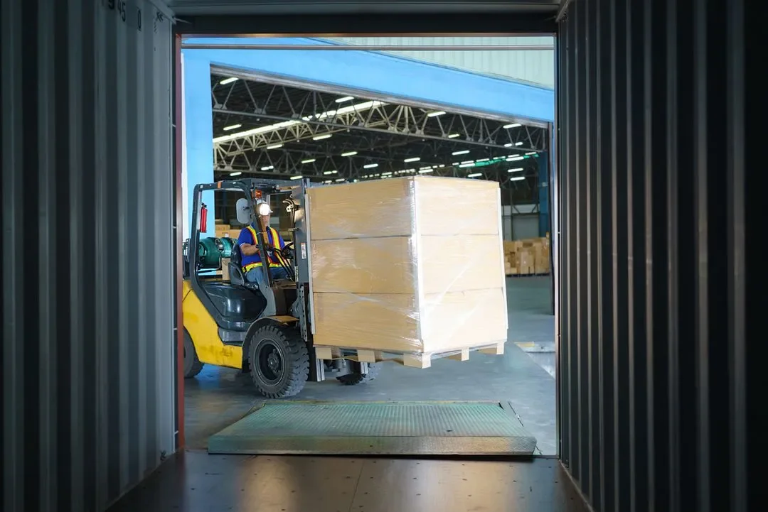 A forklift moving a large wooden crate inside a warehouse.
