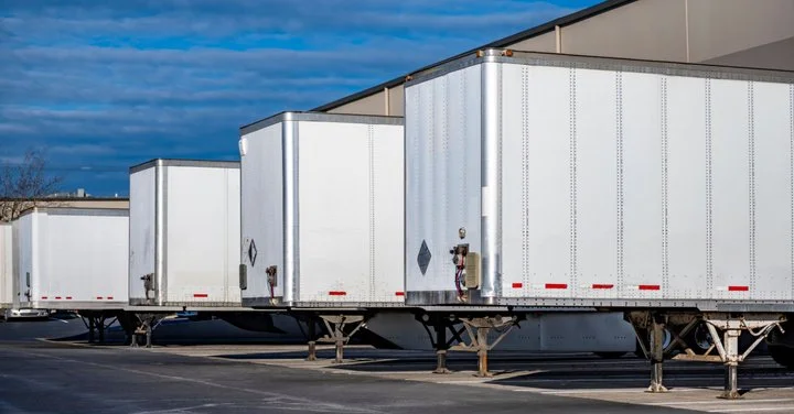 Several white semi-trailers parked in a lot against a partly cloudy sky.