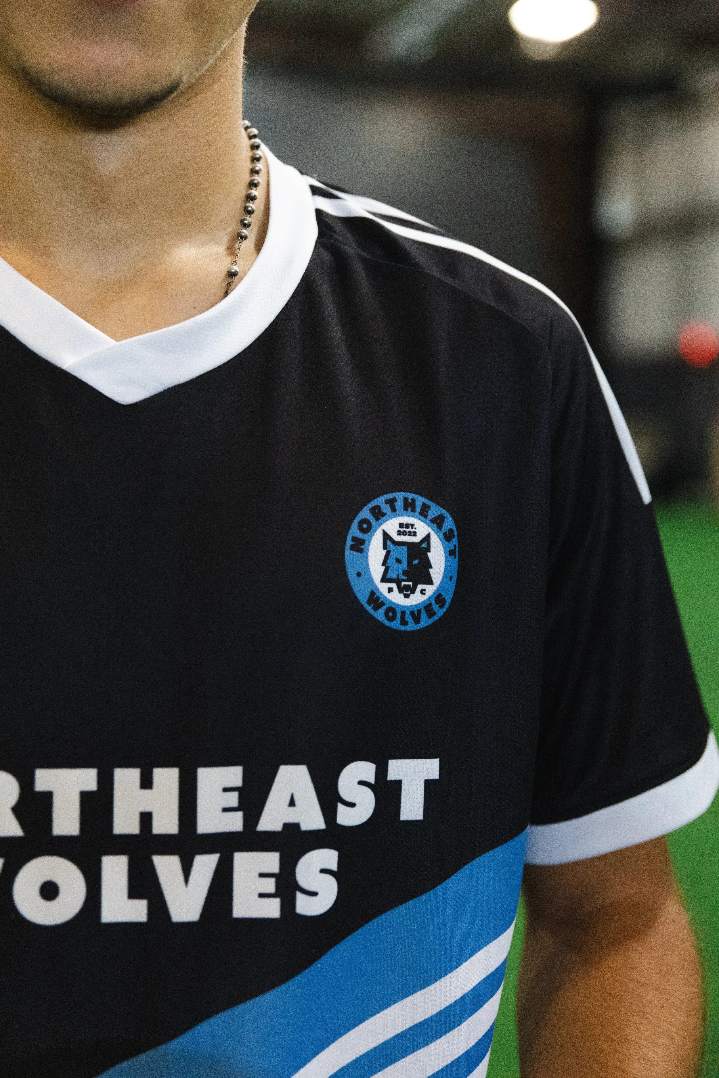 Close-up of a person wearing a black athletic jersey with white and blue accents. The jersey has a logo that says 'NORTHEAST WOLVES' and features a wolf's face. There is additional text, 'NORTHEAST' and 'WOLVES', on the front of the jersey.