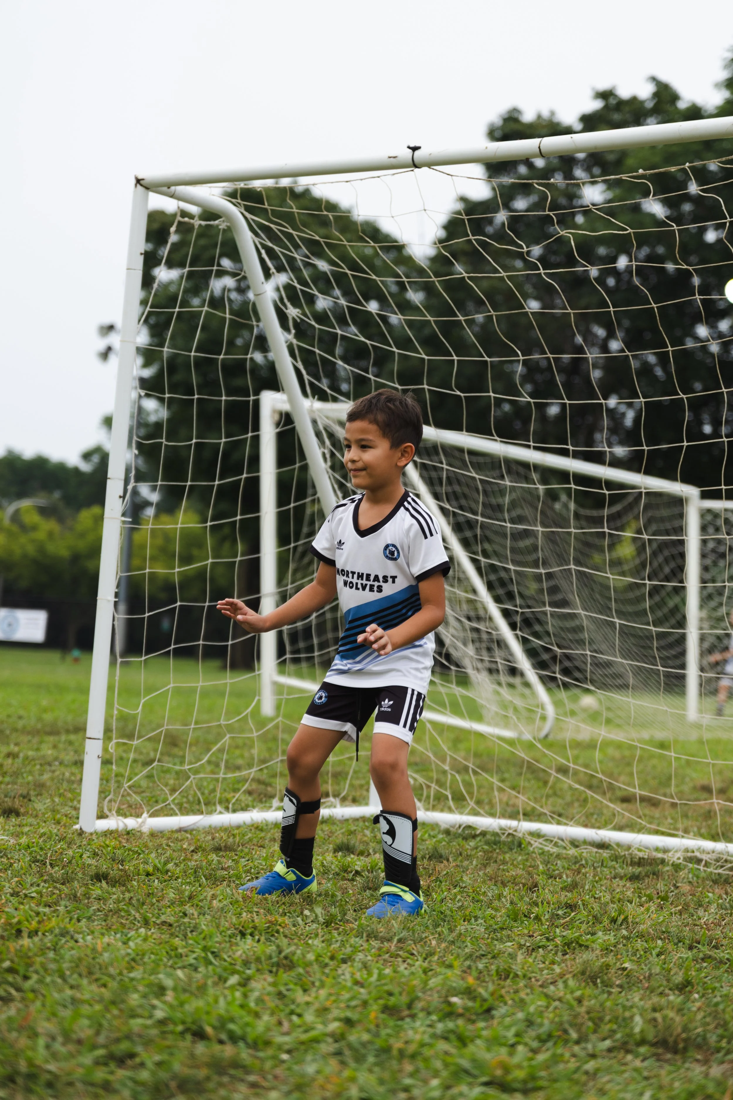 A young boy in soccer uniform standing in front of a soccer goal on a grassy field.