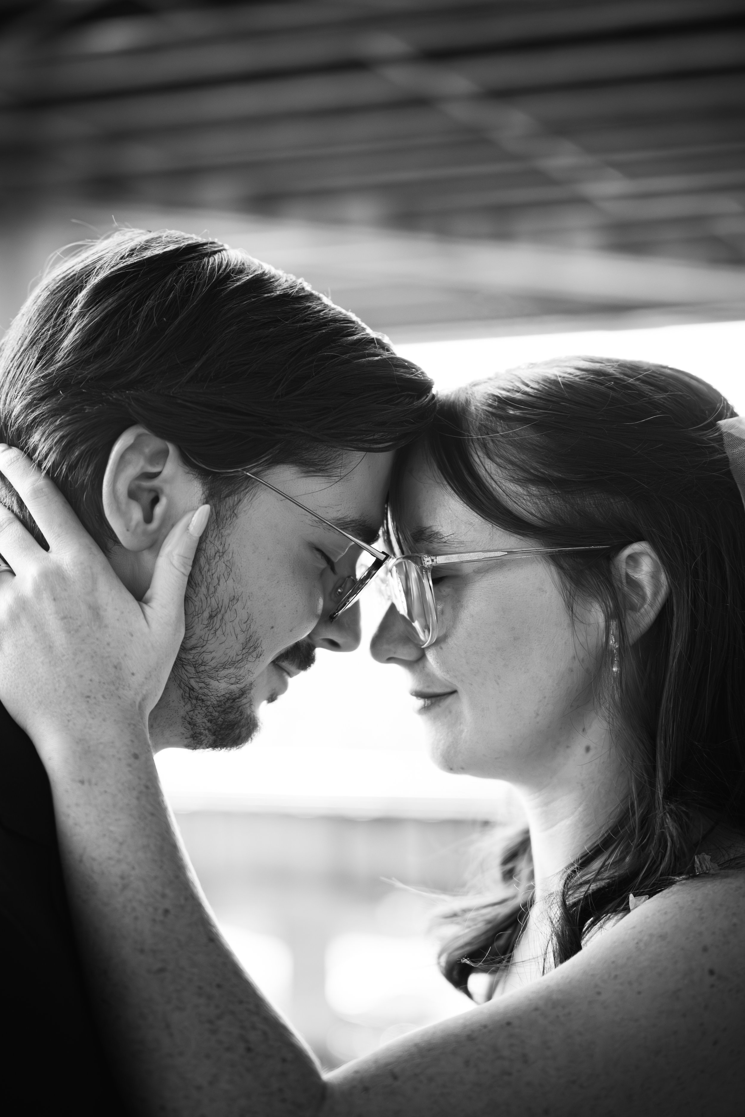 A black and white photograph of a couple with eyes closed and foreheads touching, sharing an intimate moment.