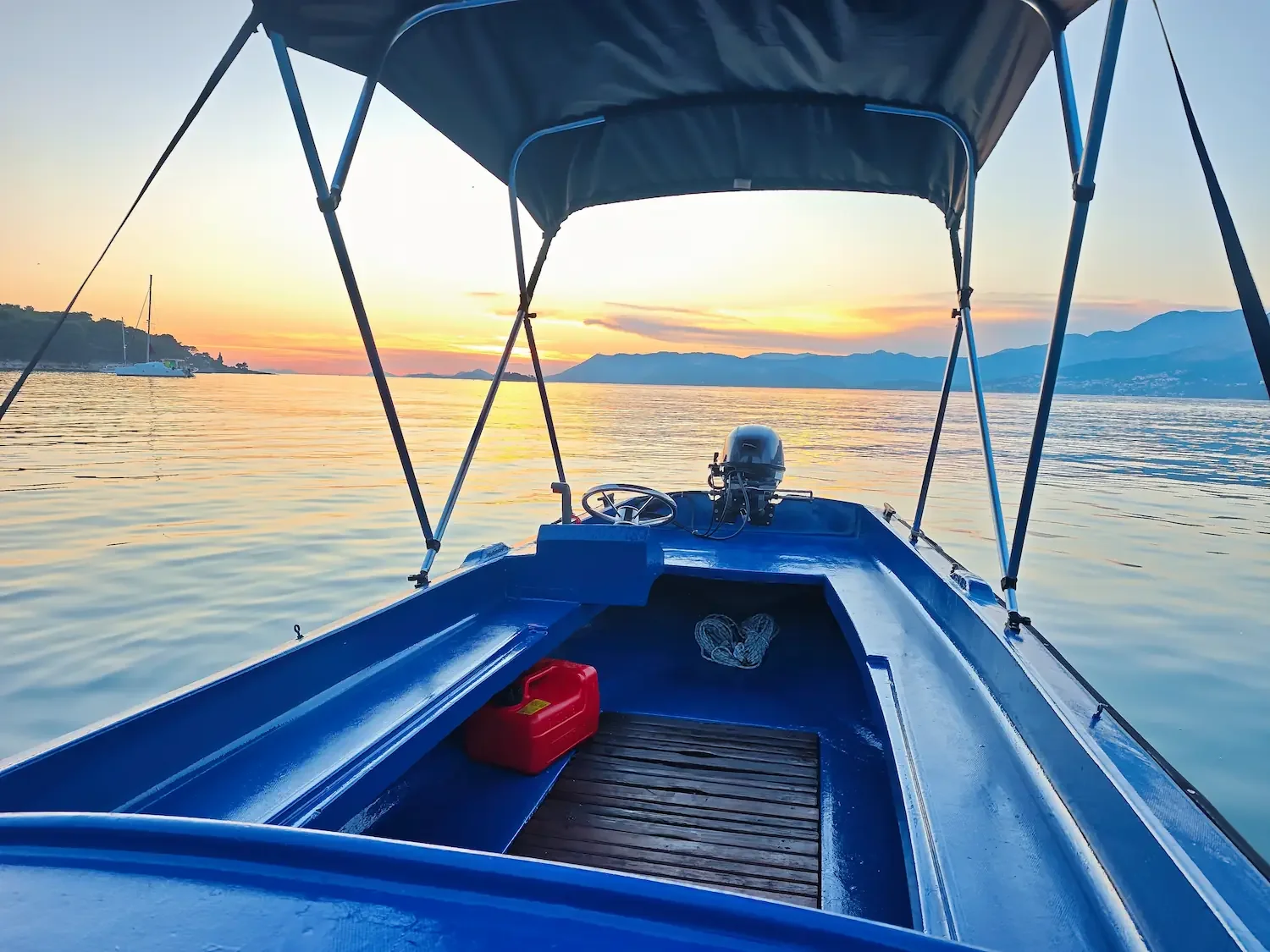 Interior view of a small rental boat with a steering wheel and bimini top during a golden sunset in Cavtat.