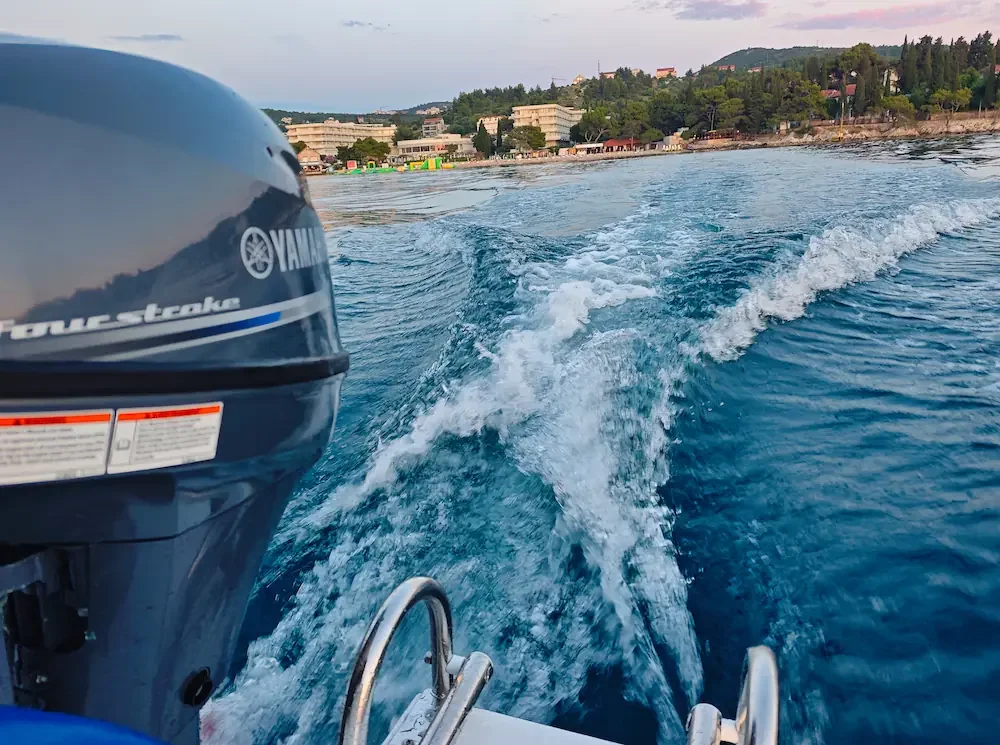 Boat wake in the blue sea behind a Yamaha outboard motor with the Cavtat coastline in the background.