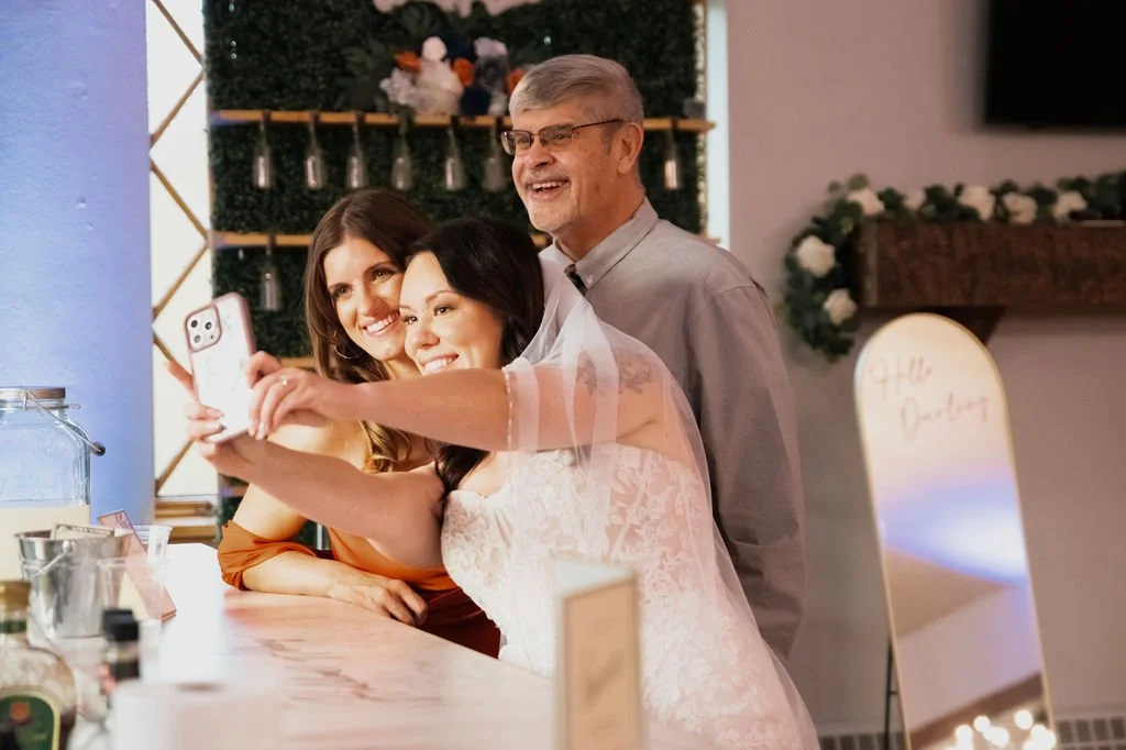 Bride takes a joyful selfie at the bar with guests during wedding reception at The Hidden Abbey. Photo taken by Karla Dooley Photography.
