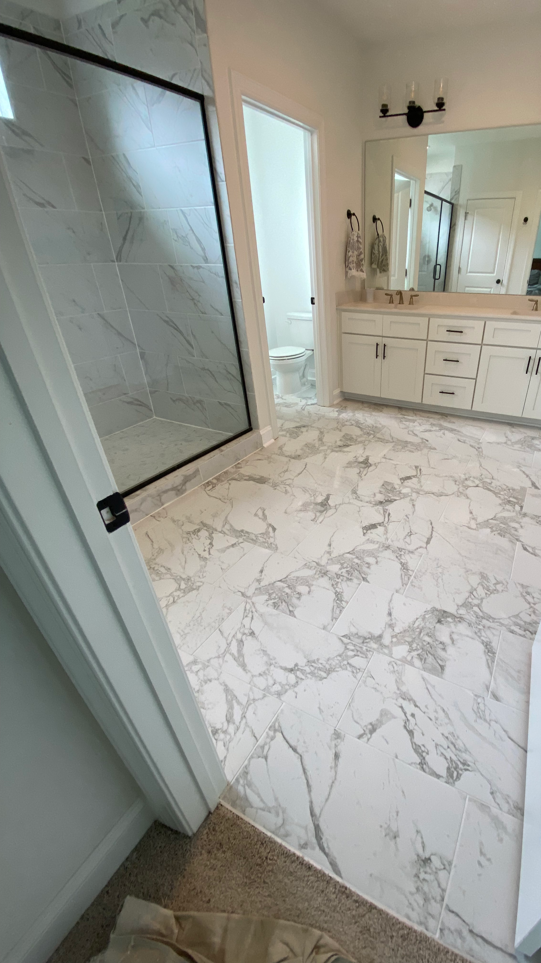 Bathroom with marble tile flooring, a glass-enclosed shower, a toilet room, and a white vanity with double sinks and mirror.