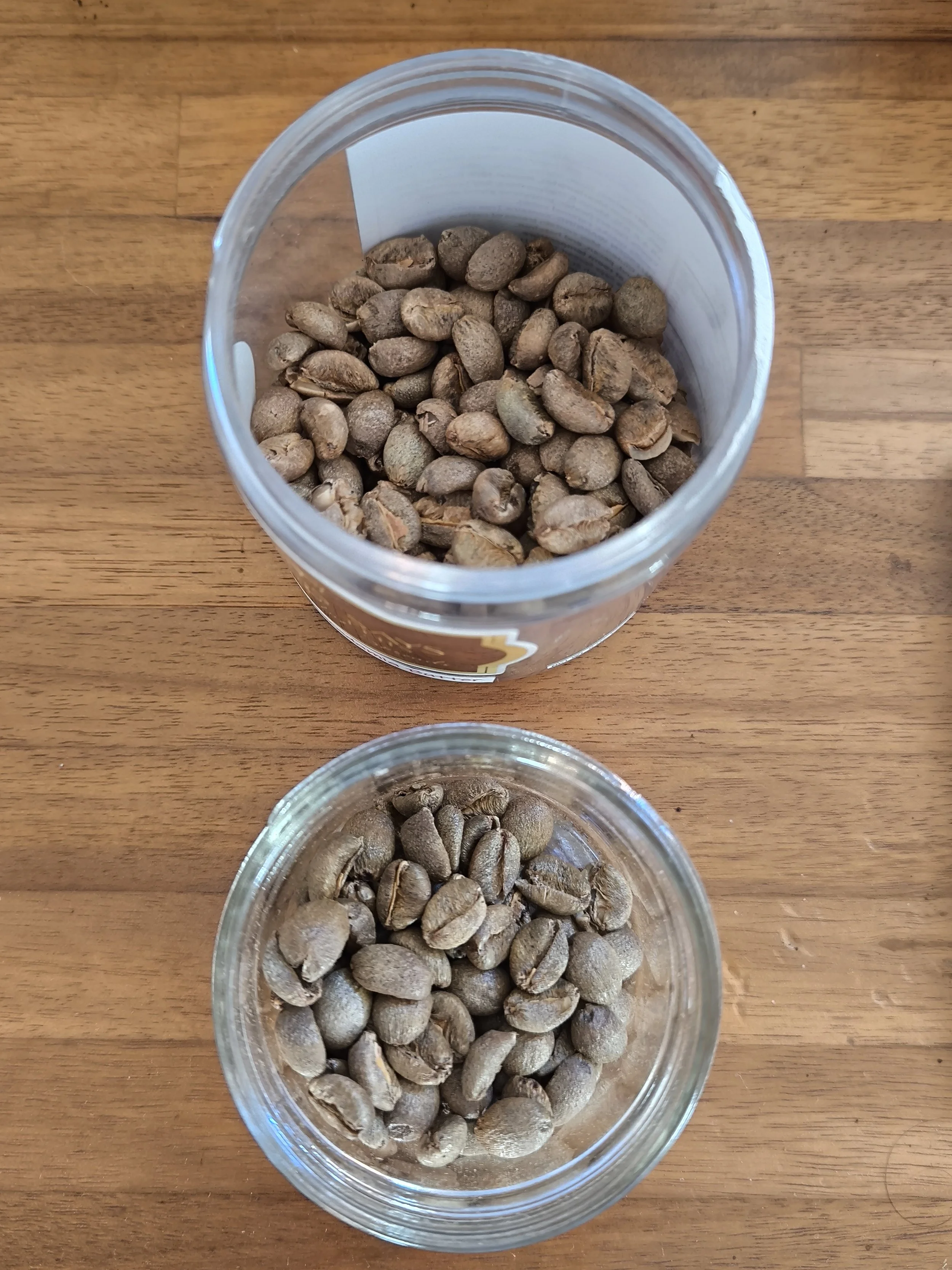 Unroasted coffee samples in two small jars on a wooden background.
