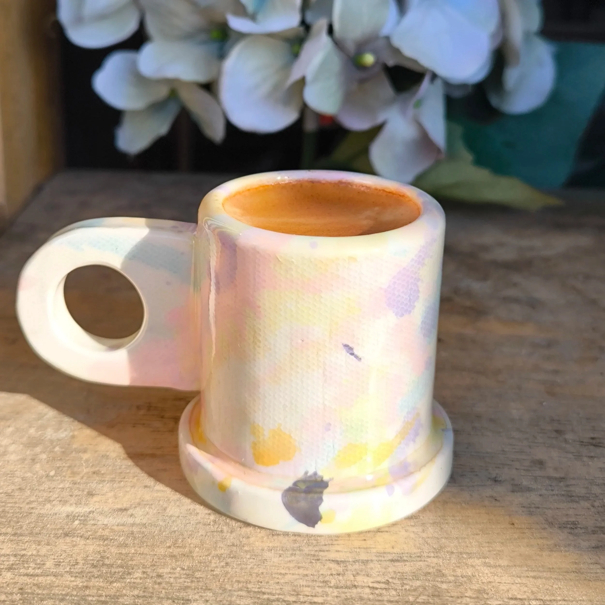 a small, colorful espresso cup with flat handle with a circle in it.