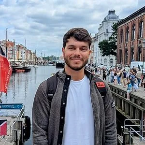 Ragazzo sorridente in una zona turistica vicino a un canale con edifici storici, persone e bar lungo il fiume.