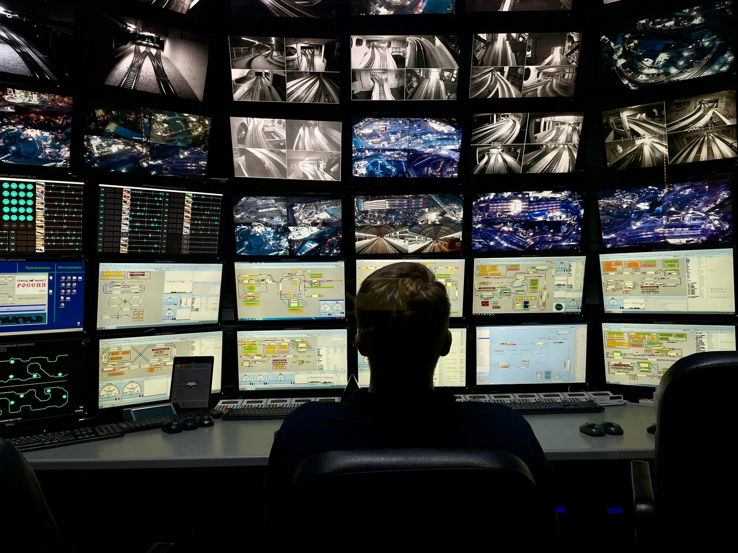 A person sitting in front of multiple monitors reviewing various surveillance camera feeds and diagrams.