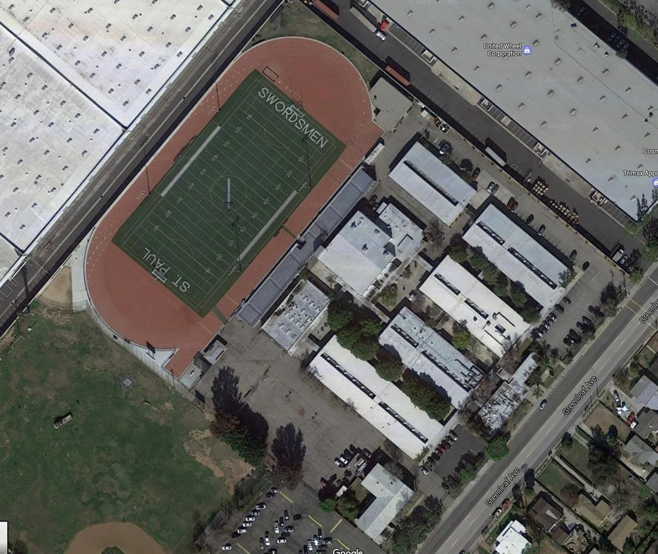 Overhead view of a campus with a football field surrounded by buildings, parking lots and a street.