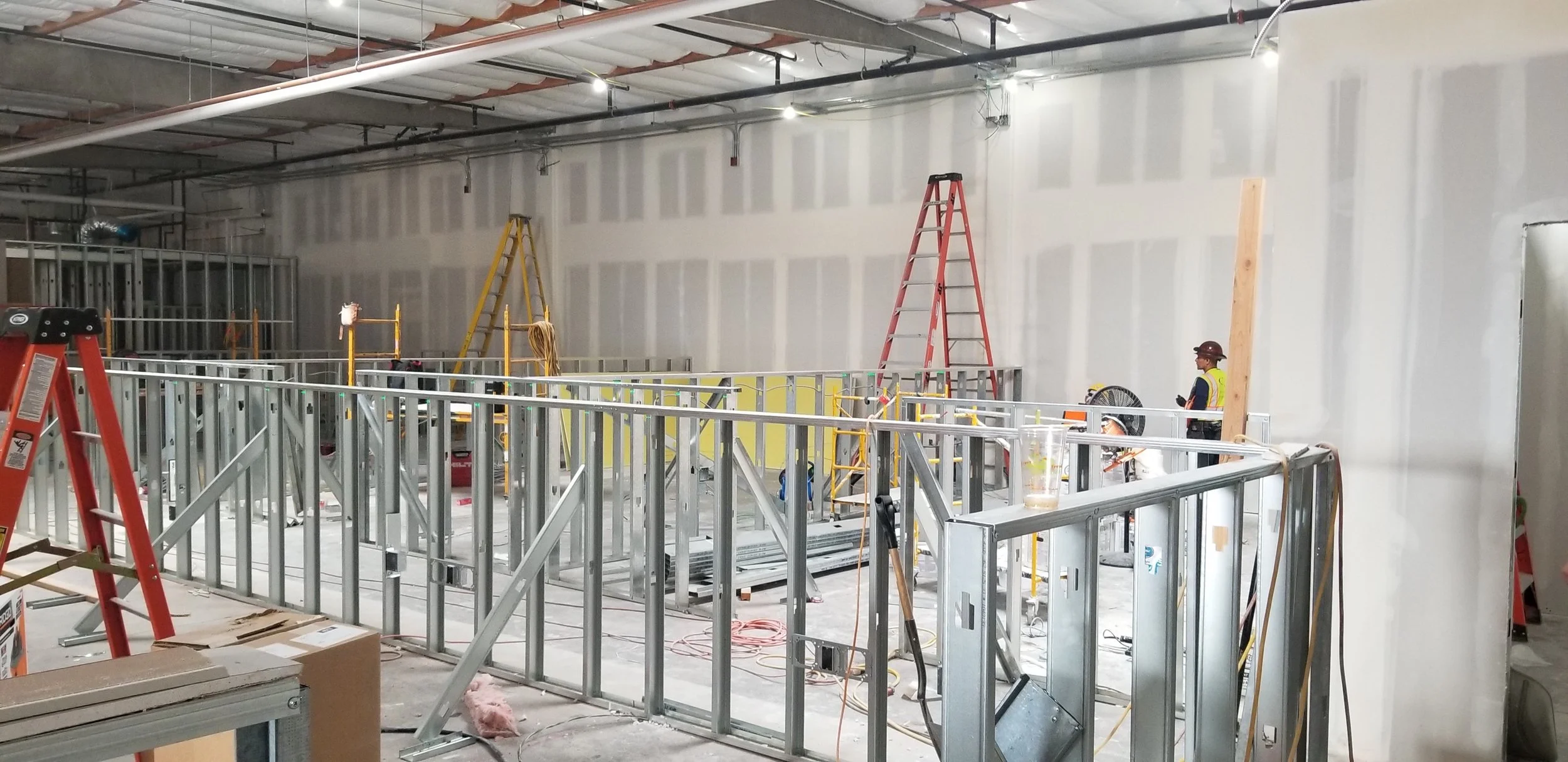 Construction building interior framework with metal studs, ladders and tools in an unfinished commercial space.