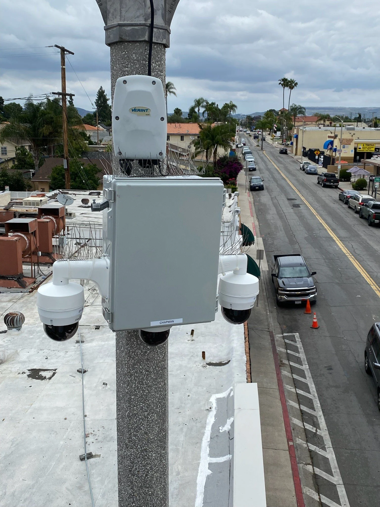 Light Post Camera Solutions equipment mounted on a pole with a city street in the background, including parked cars, palm trees and buildings.