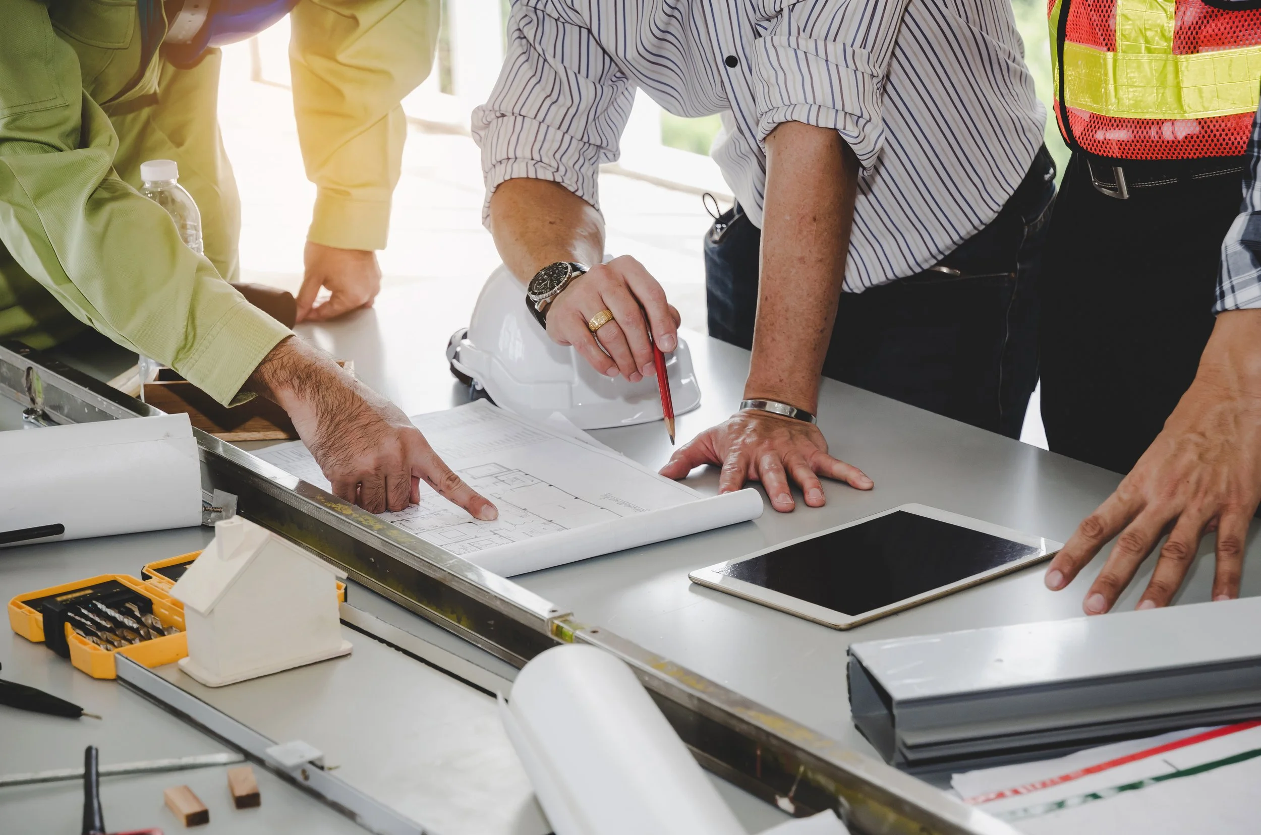 People gathered around a table looking at architectural blueprints, with tools and construction plans on the table.