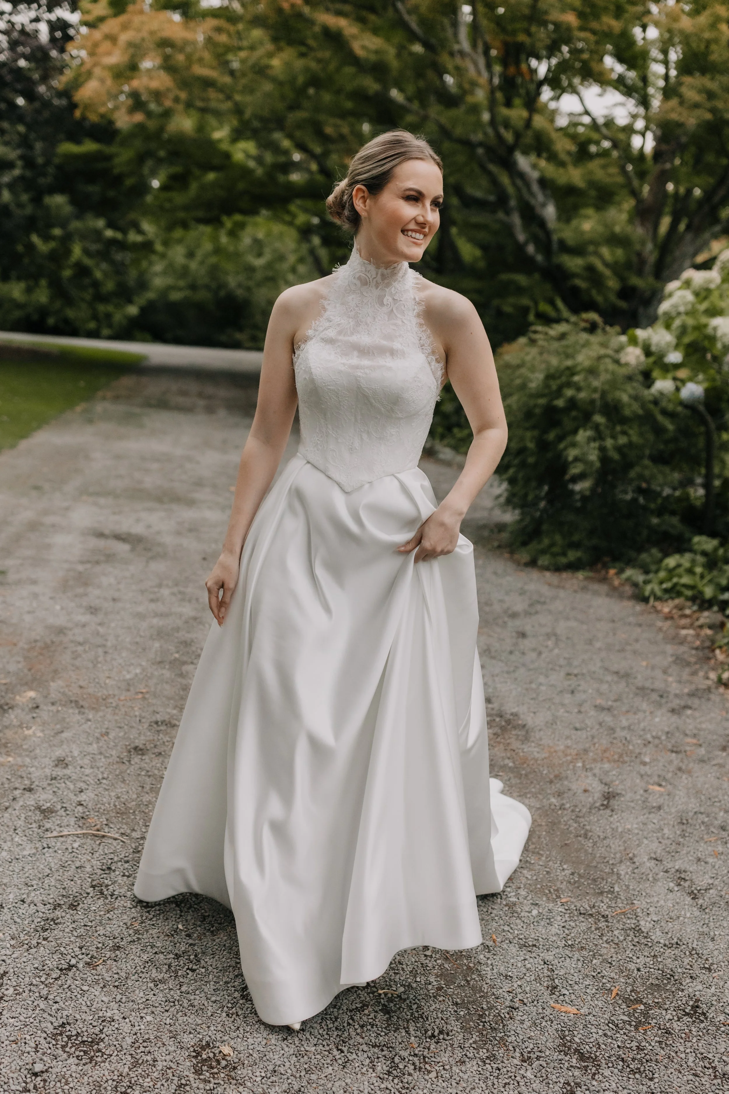 A woman in a white off-shoulder wedding dress standing in front of white curtains.