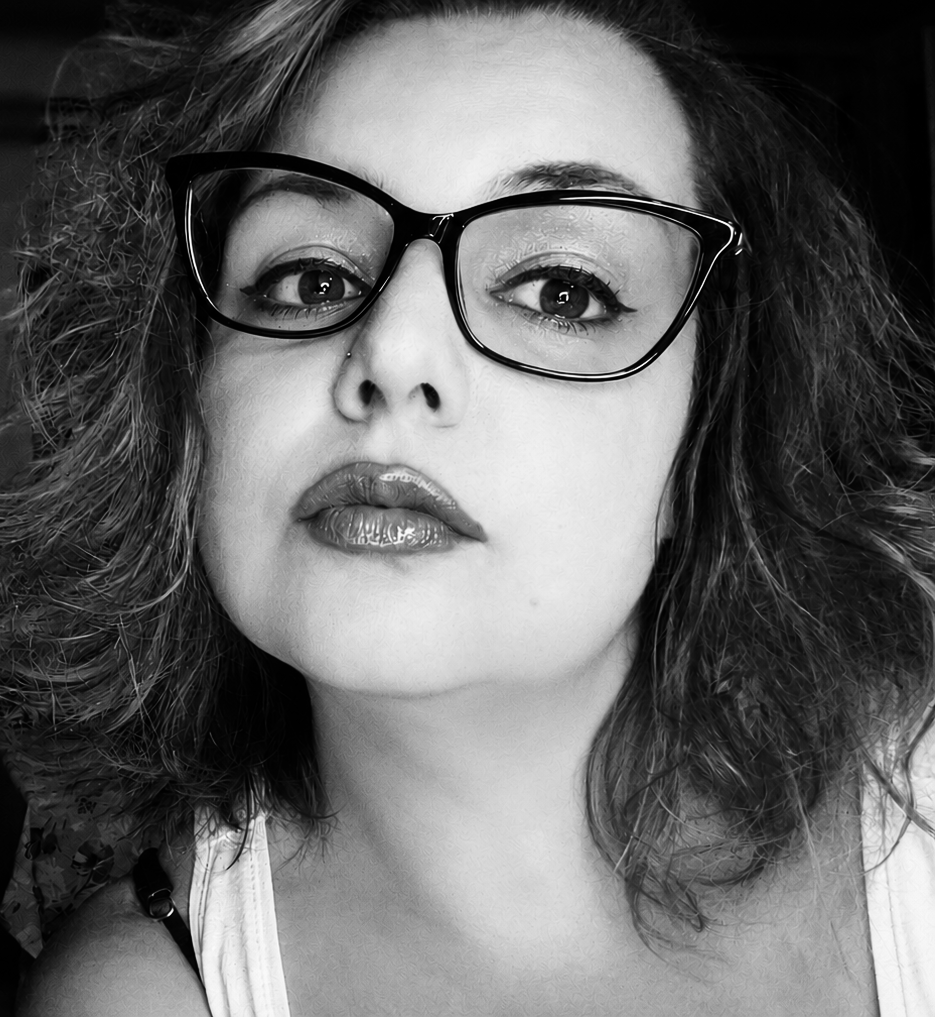 A black and white close-up portrait of a woman wearing glasses, with voluminous curly hair and makeup.