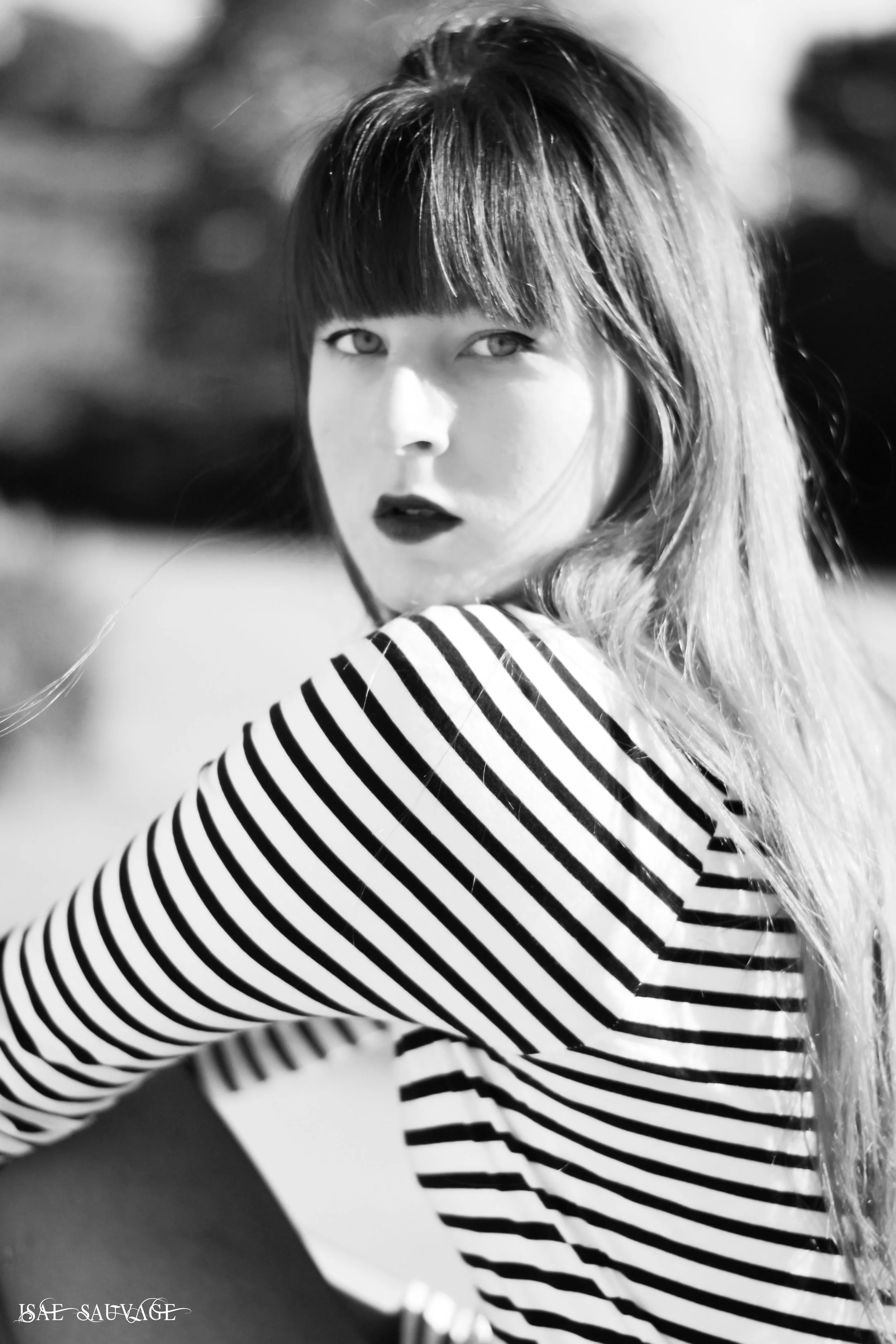 Une femme avec des cheveux bruns, portant un pull à rayures noires et blanches, regarde par-dessus son épaule dans une photo en noir et blanc.