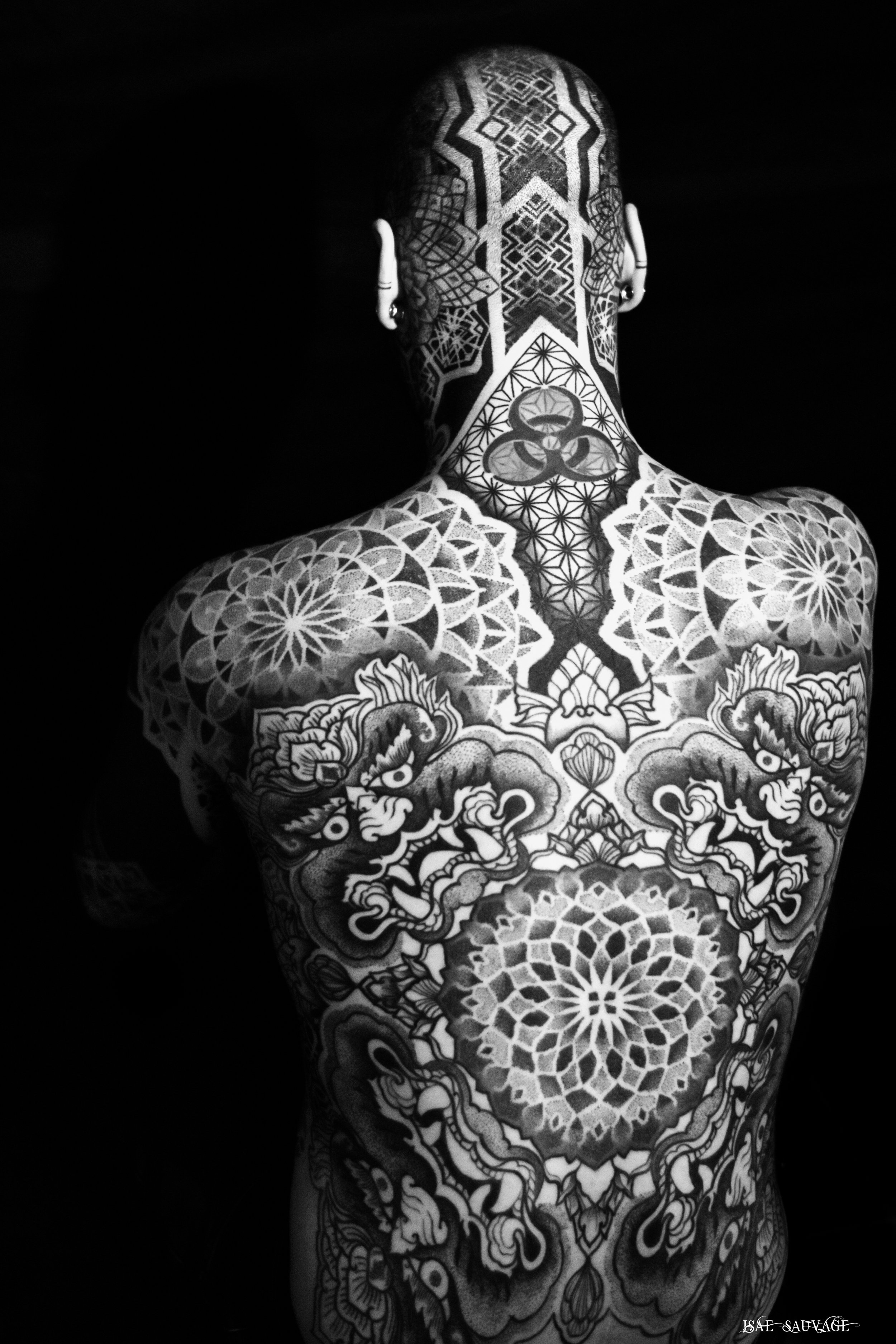 Un homme vu de dos, entièrement recouvert de tatouages de style traditionnel japonais en noir et blanc, posant contre un fond noir.