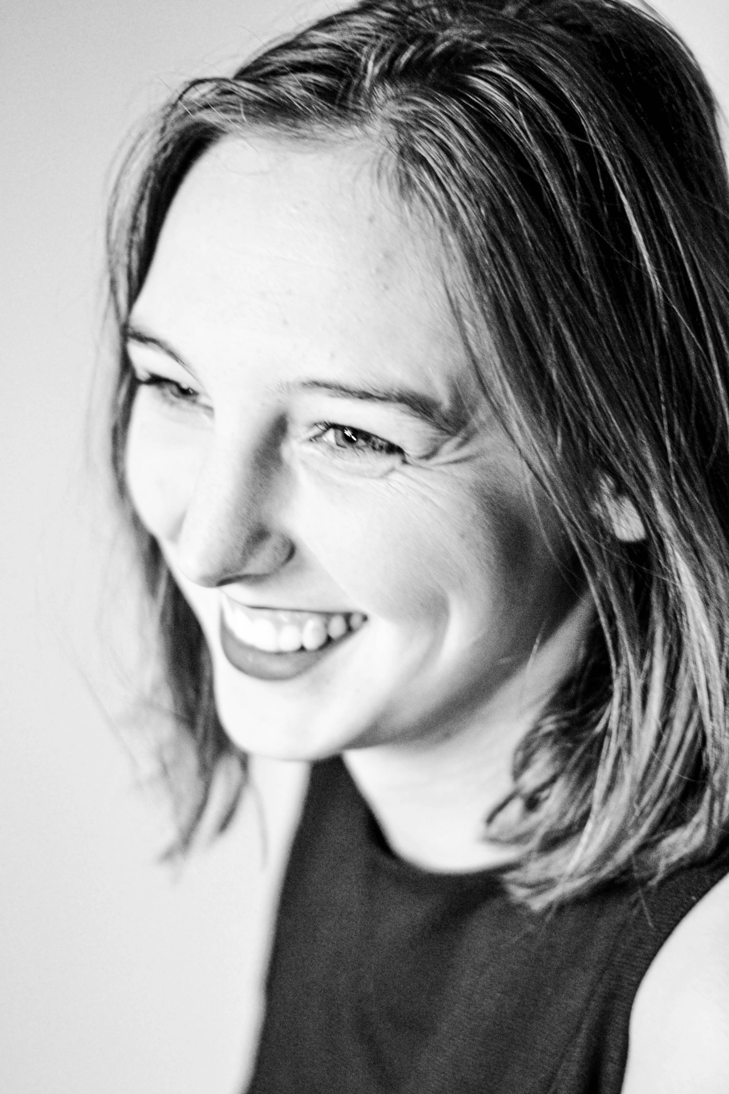 Portrait en noir et blanc d'une femme souriante avec des cheveux longs, coiffés en arrière, portant un haut sombre, regardant légèrement vers la gauche.