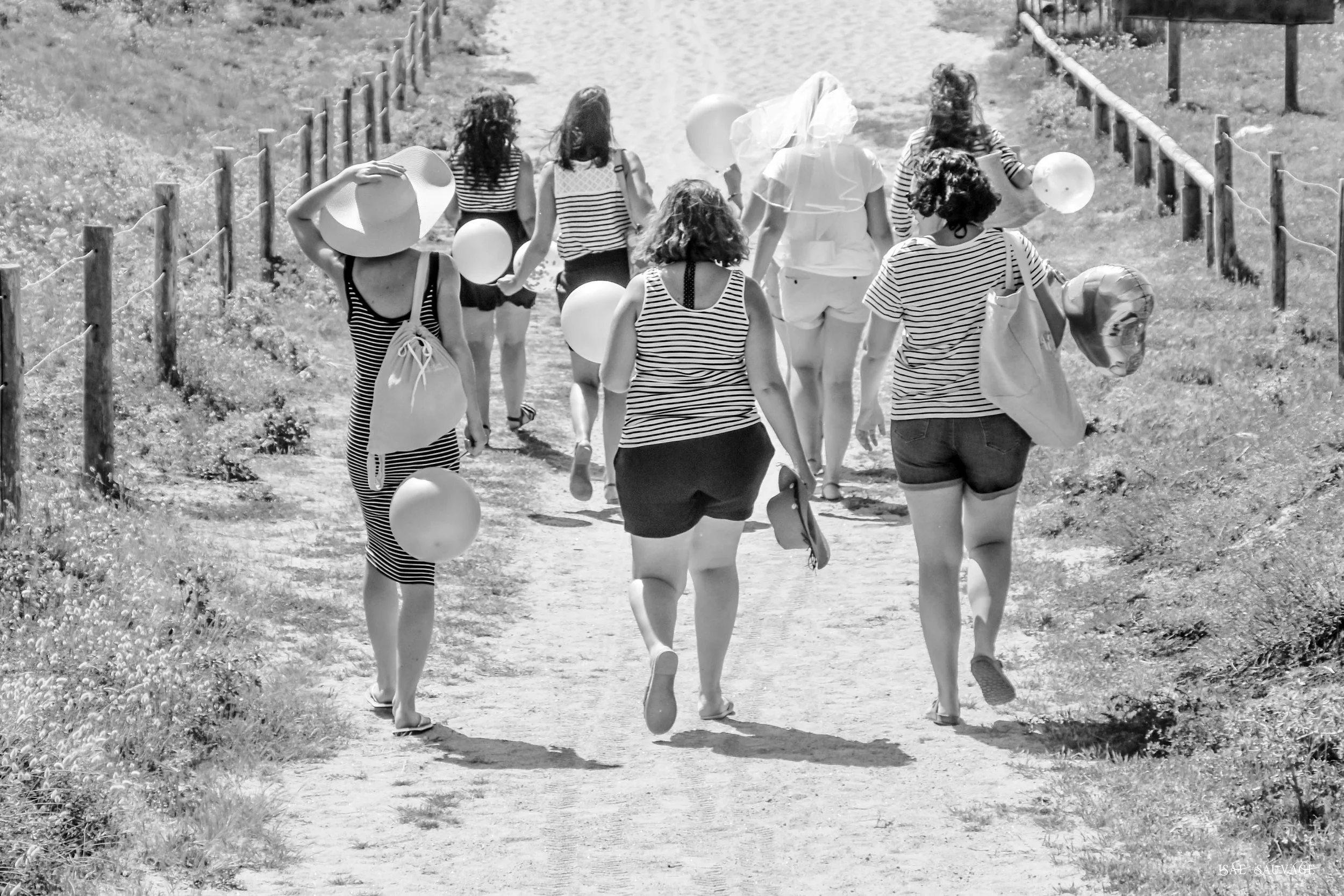 Groupe de femmes marchant sur un chemin de terre, portant des ballons et des chapeaux, habillées de marinières, en plein air.