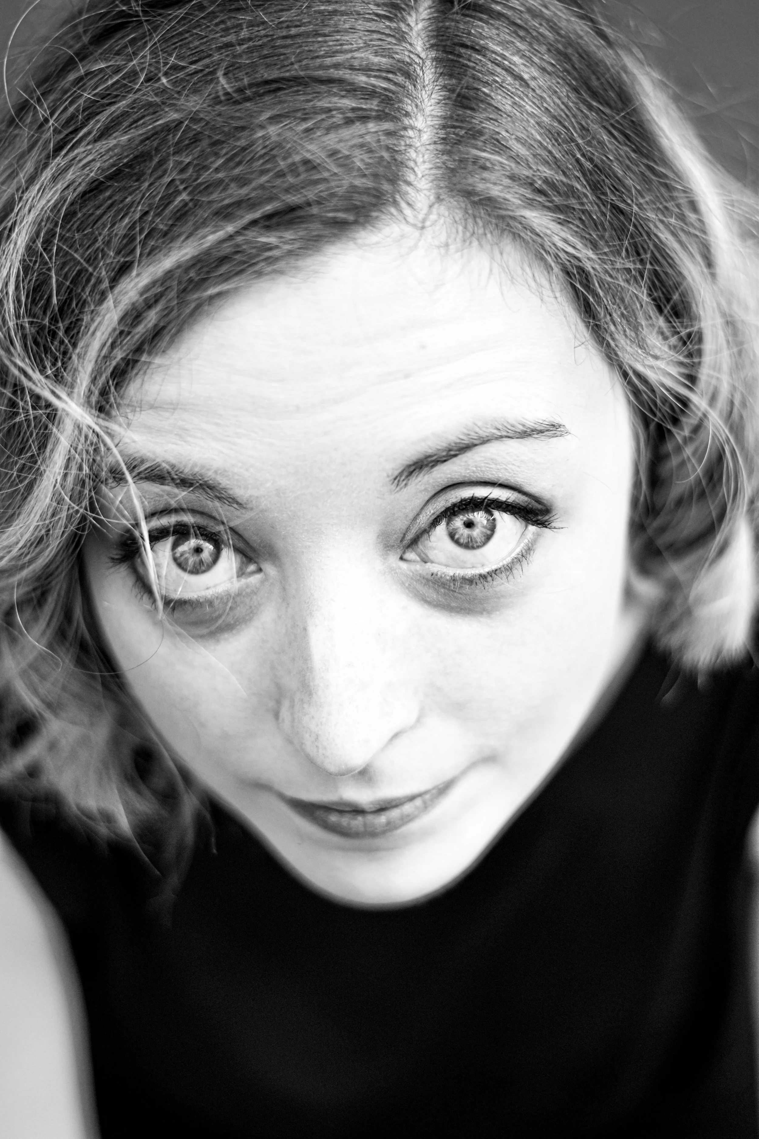 Un portrait en noir et blanc d'une femme avec des cheveux bouclés clair, regardant vers le haut avec un sourire léger.