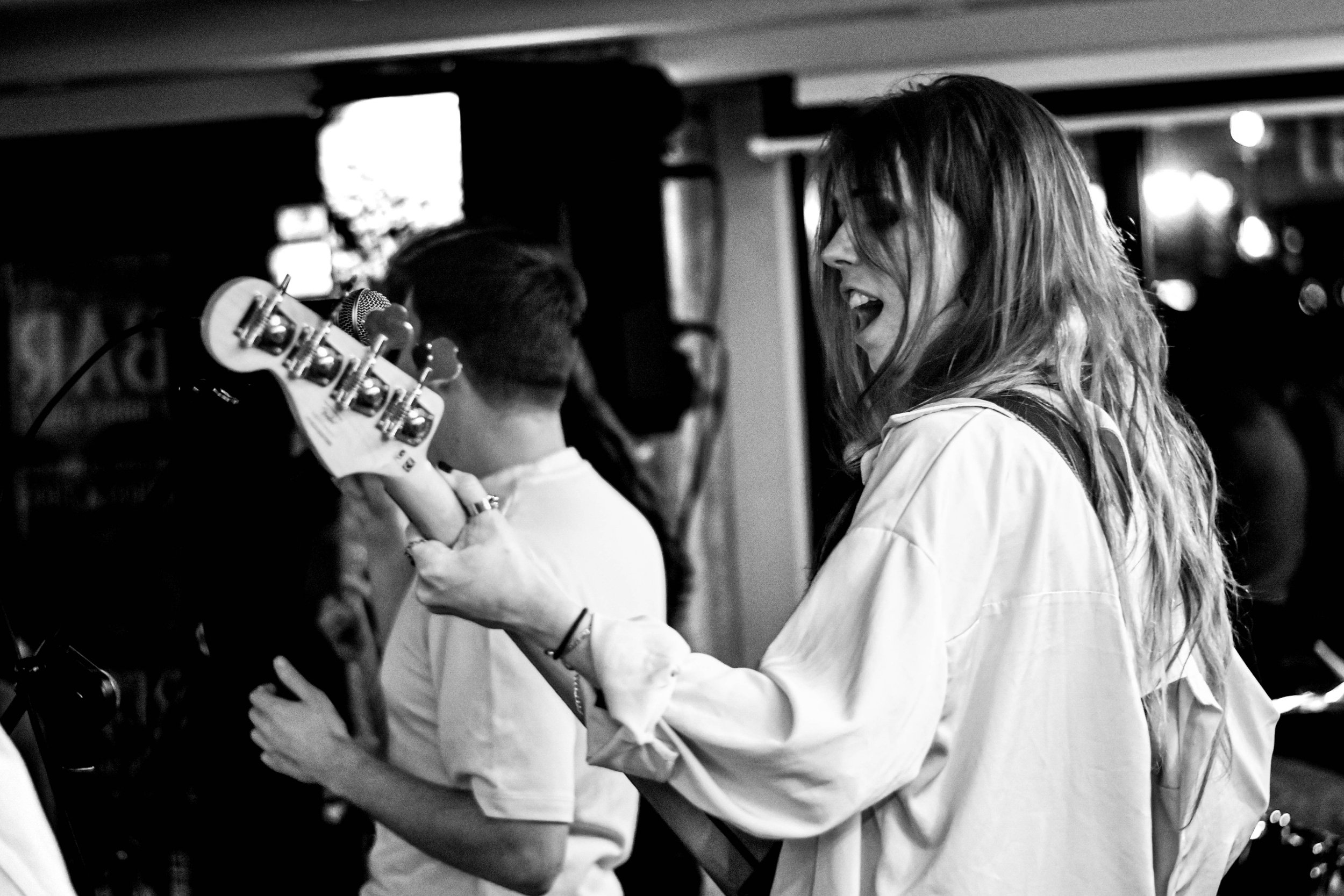 Deux personnes dans une ambiance de concert, une femme avec long cheveux bouclés chantant et jouant de la basse face à un public. 