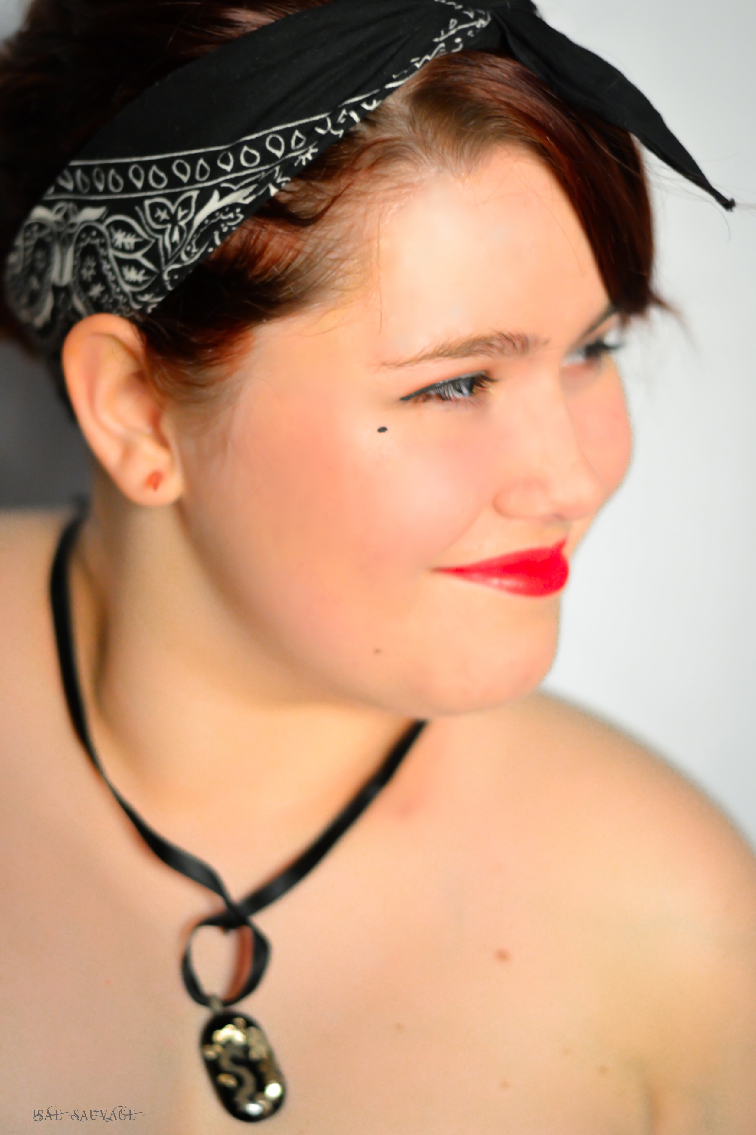 Portrait d'une femme avec un bandana noir à motifs blancs, maquillage rouge à lèvres et collier avec pendentif.