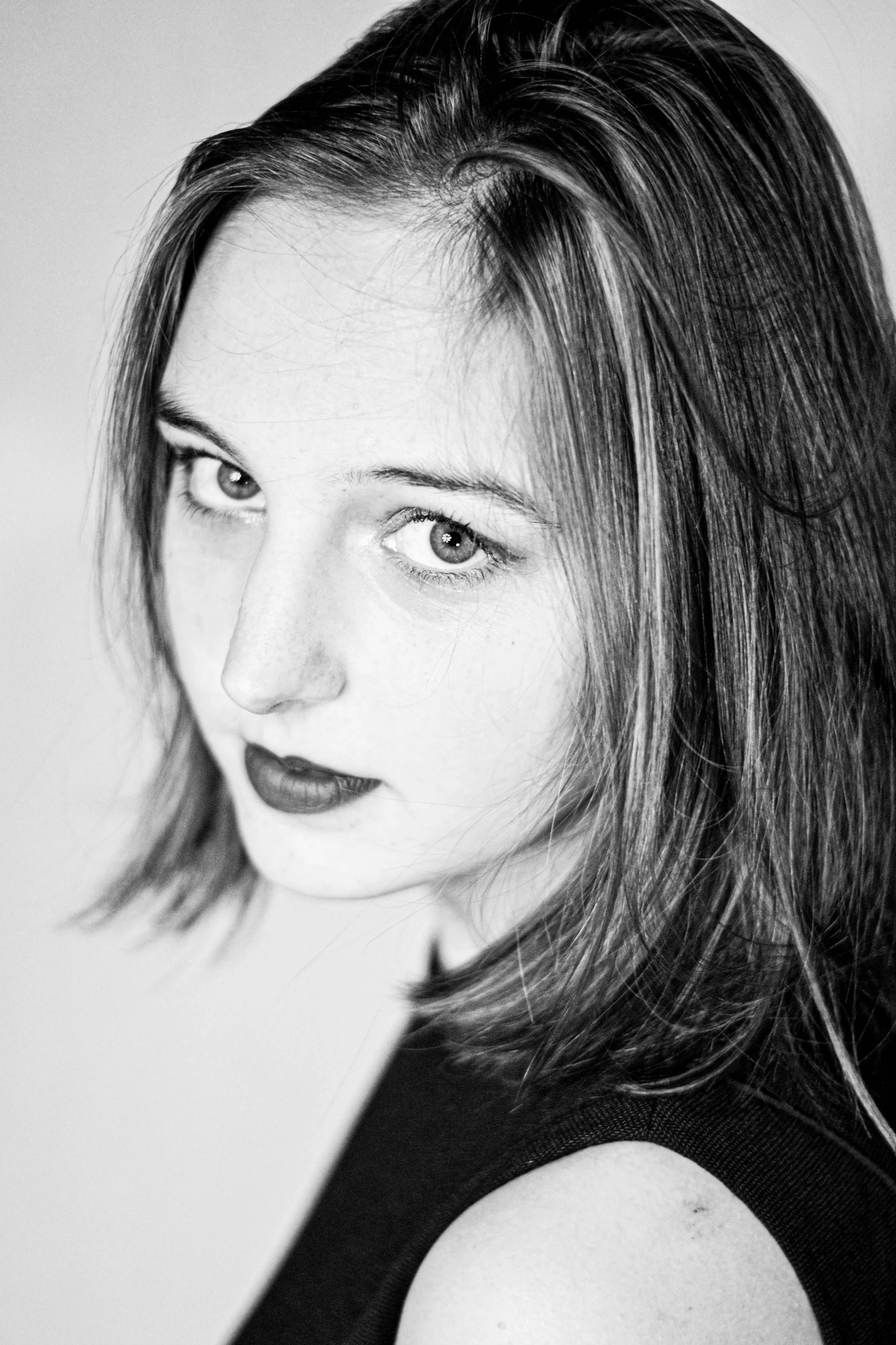 Un portrait en noir et blanc d'une femme avec des cheveux longs et légèrement ondulés, regardant vers le haut, portant un haut noir à manches courtes.