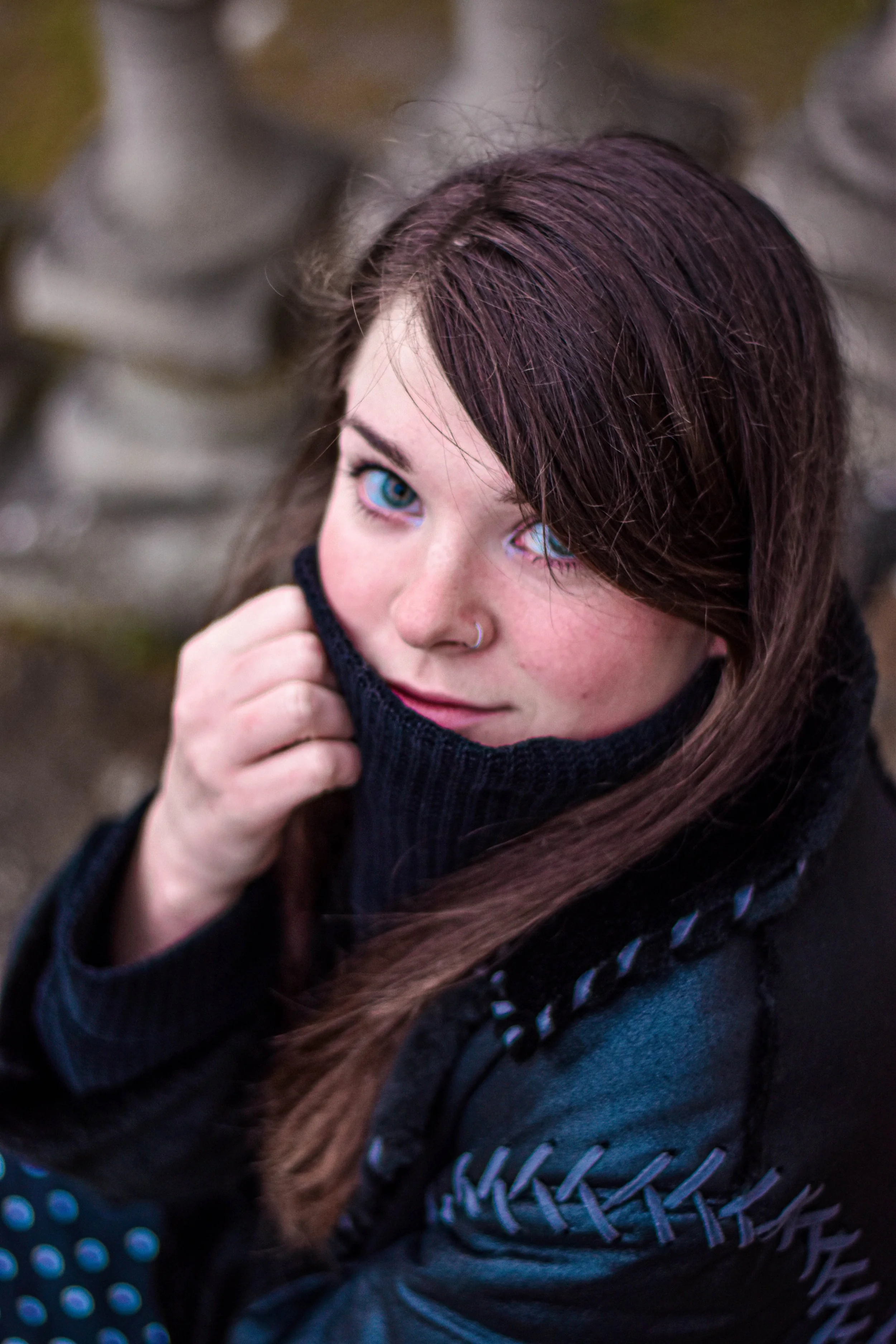 Jeune femme aux cheveux auburn, portant un pull noir, sortant une écharpe dans un environnement extérieur naturel.