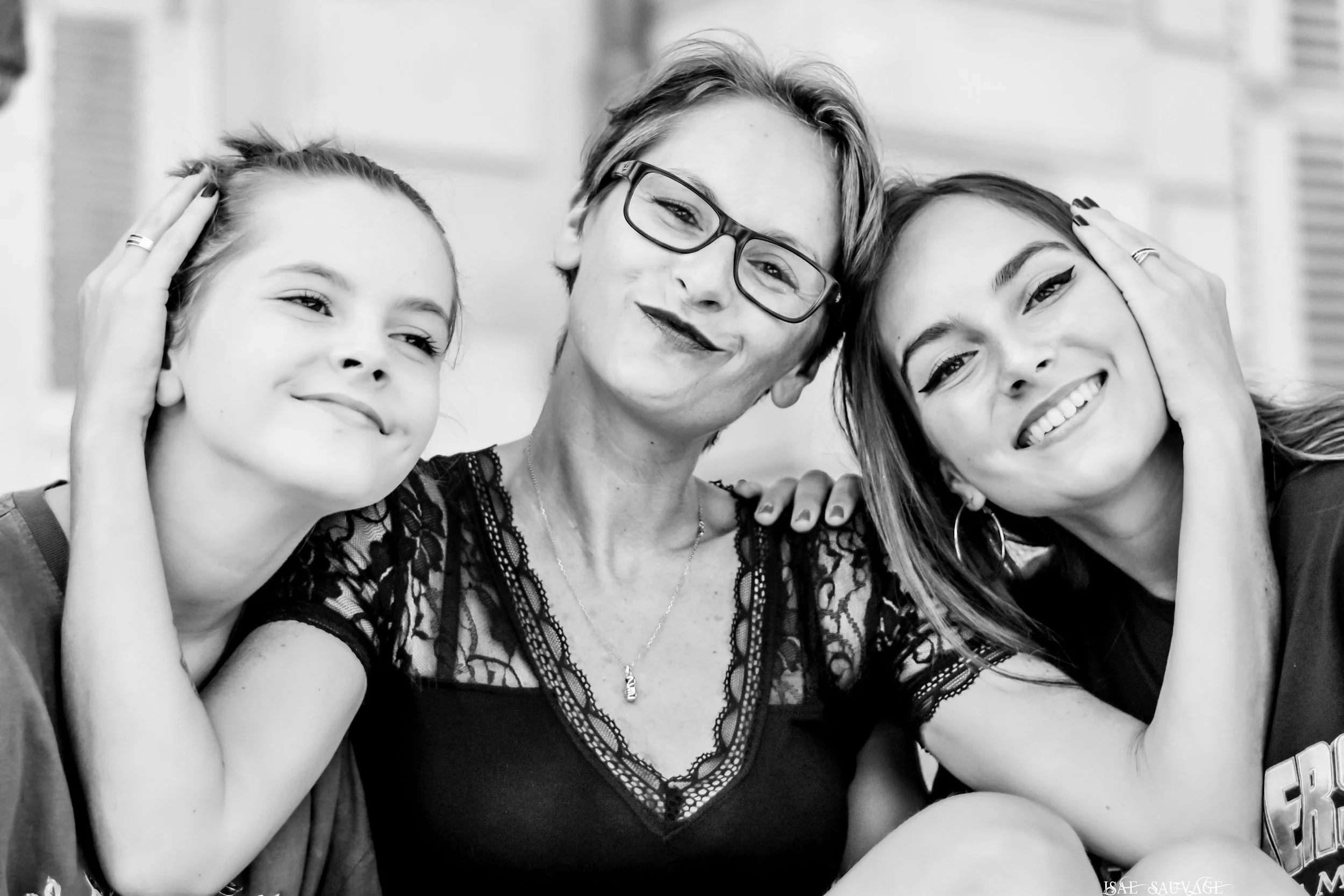 Trois femmes souriantes en gros plan, se tenant près les unes des autres, avec la main dans les cheveux, en noir et blanc.