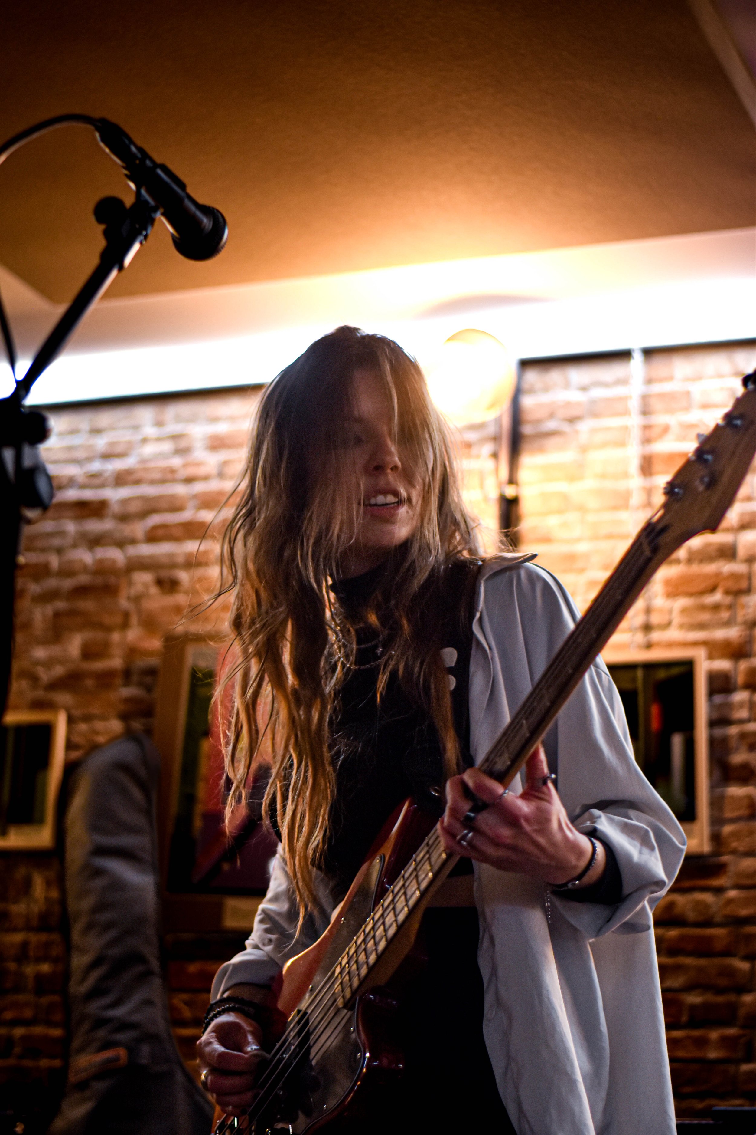 Jeune femme jouant de la guitare électrique lors d'un concert dans un lieu avec murs en briques et éclairage chaud.