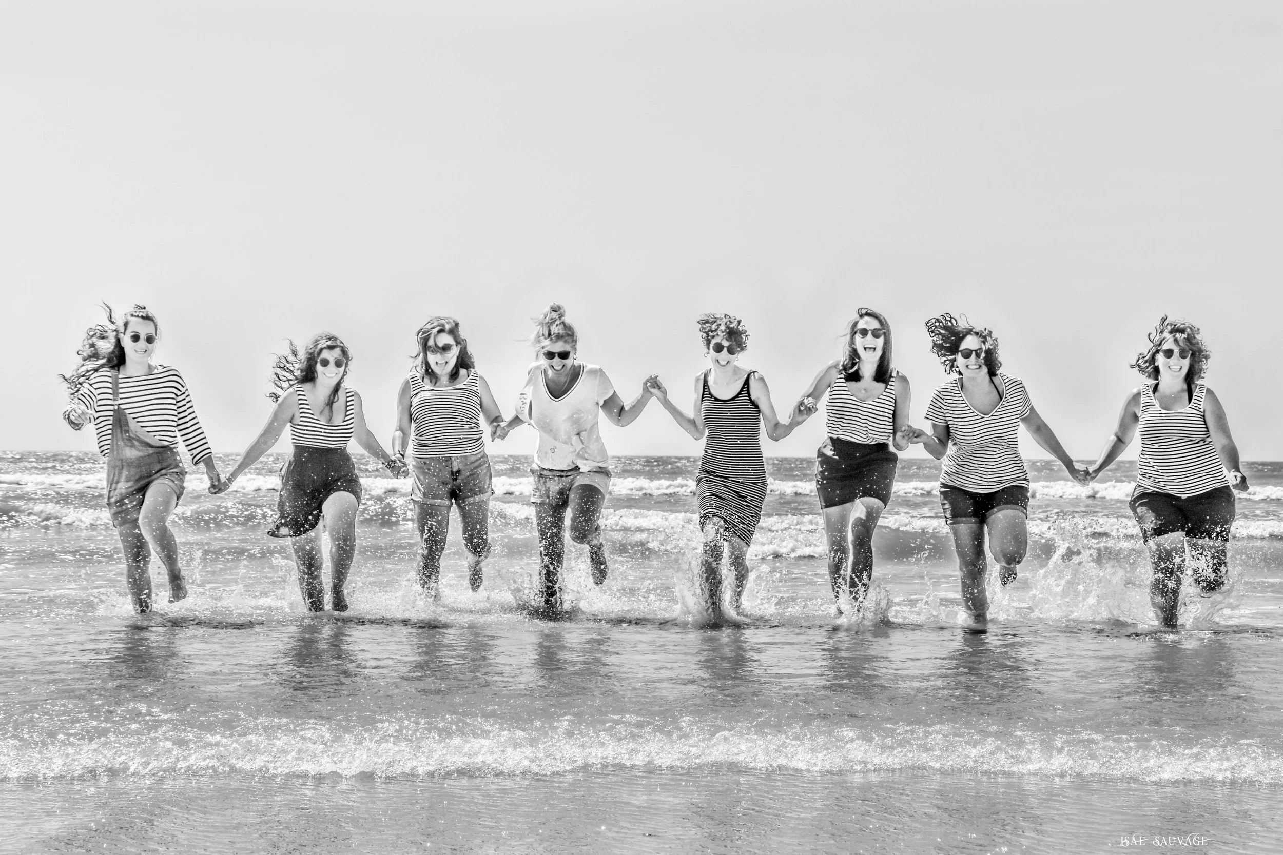 Groupe de femmes souriantes portant des vêtements marins, courant main dans la main dans la mer