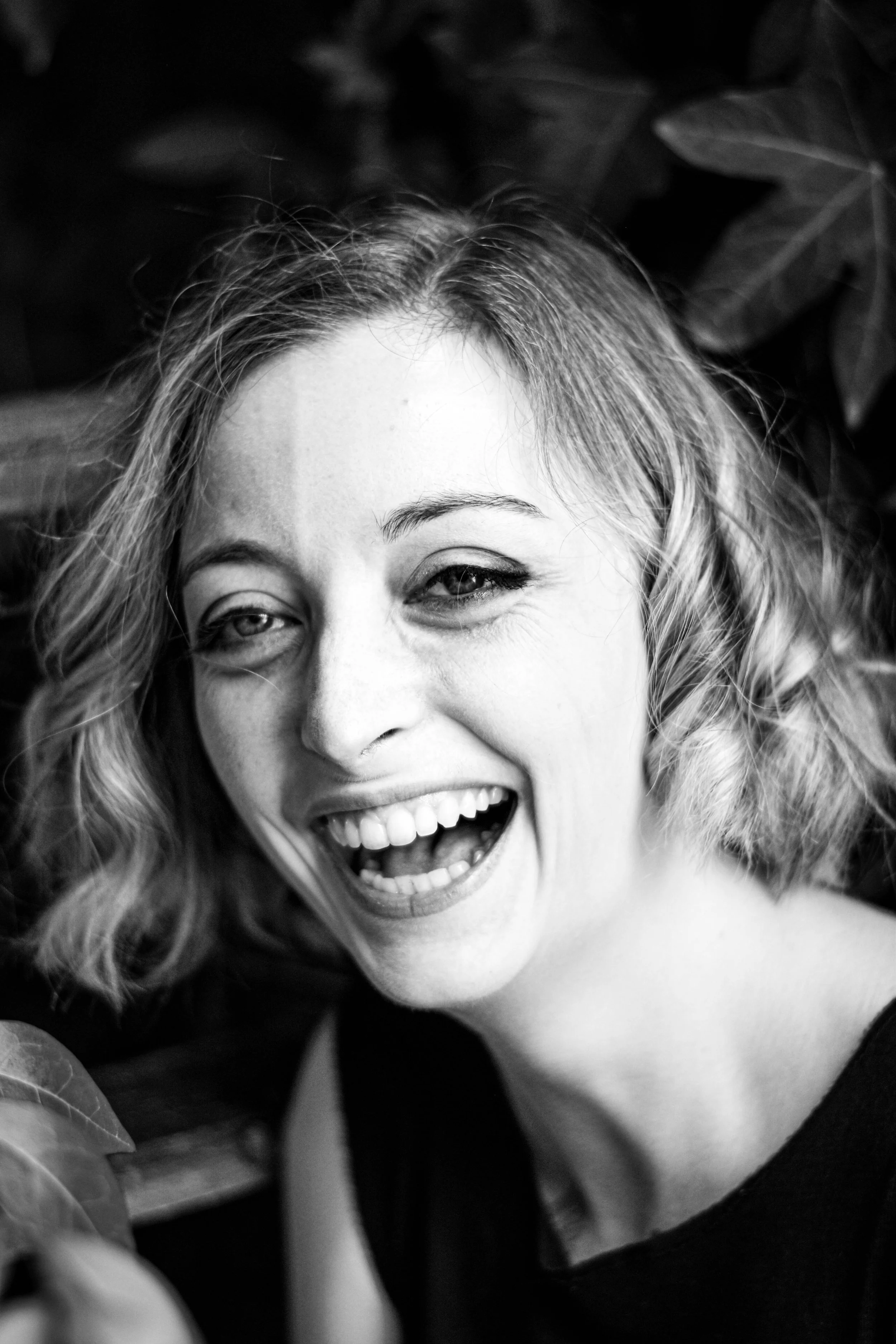Une femme souriante avec des cheveux bouclés, rigolant, entourée de feuilles.