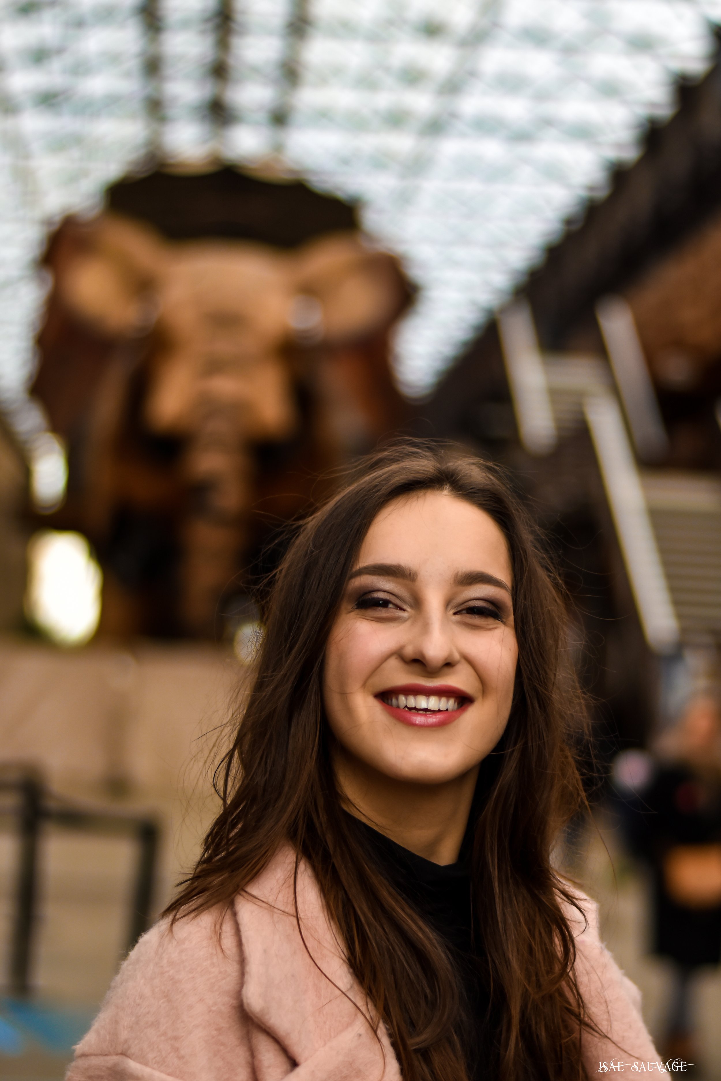 Une jeune femme souriante avec des cheveux longs bruns, portant un manteau rose clair, sous les nefs de l'Eléphant à Nantes