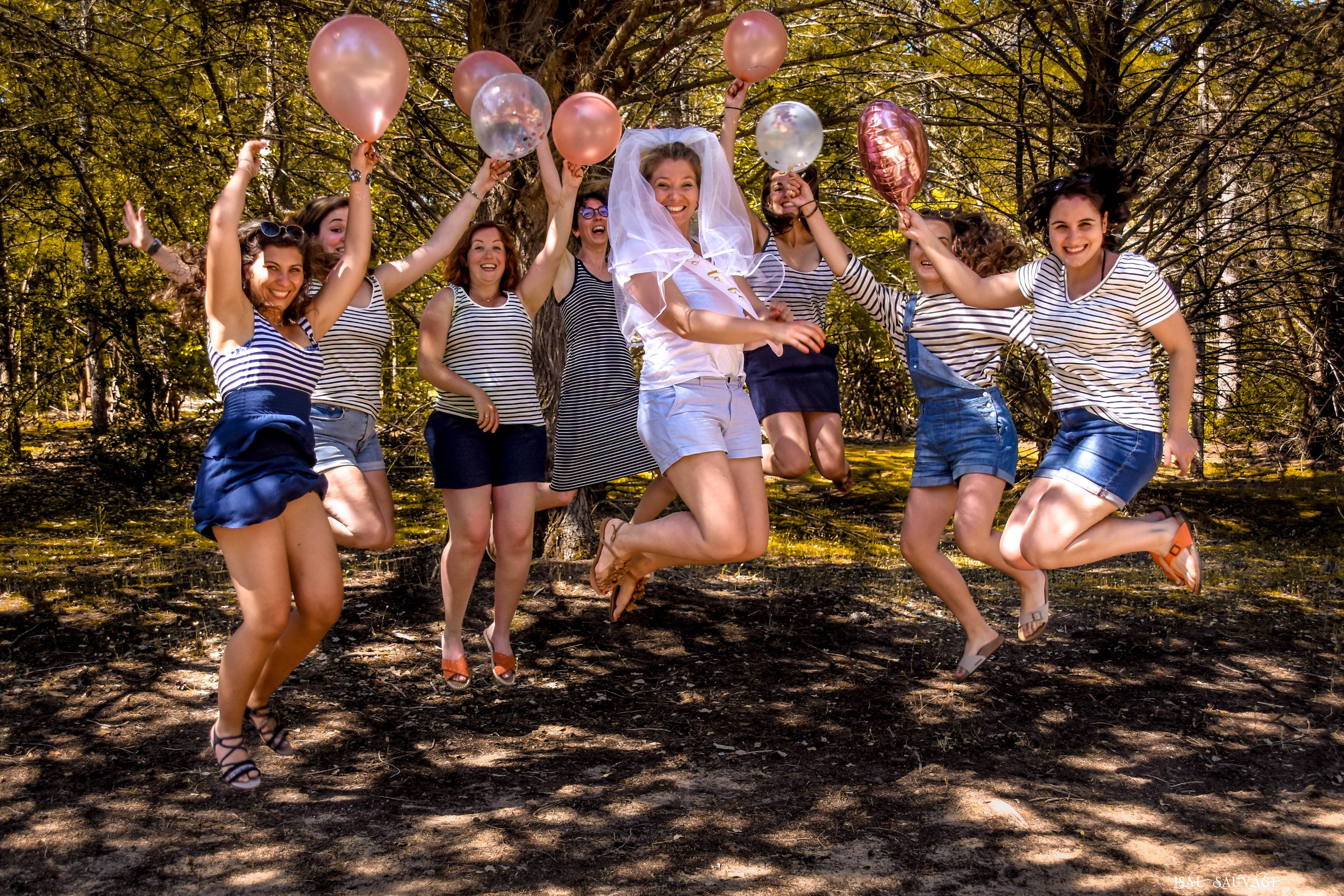 Groupe de femmes souriantes qui sautent dans les airs dans une forêt avec des ballons rose et transparent.