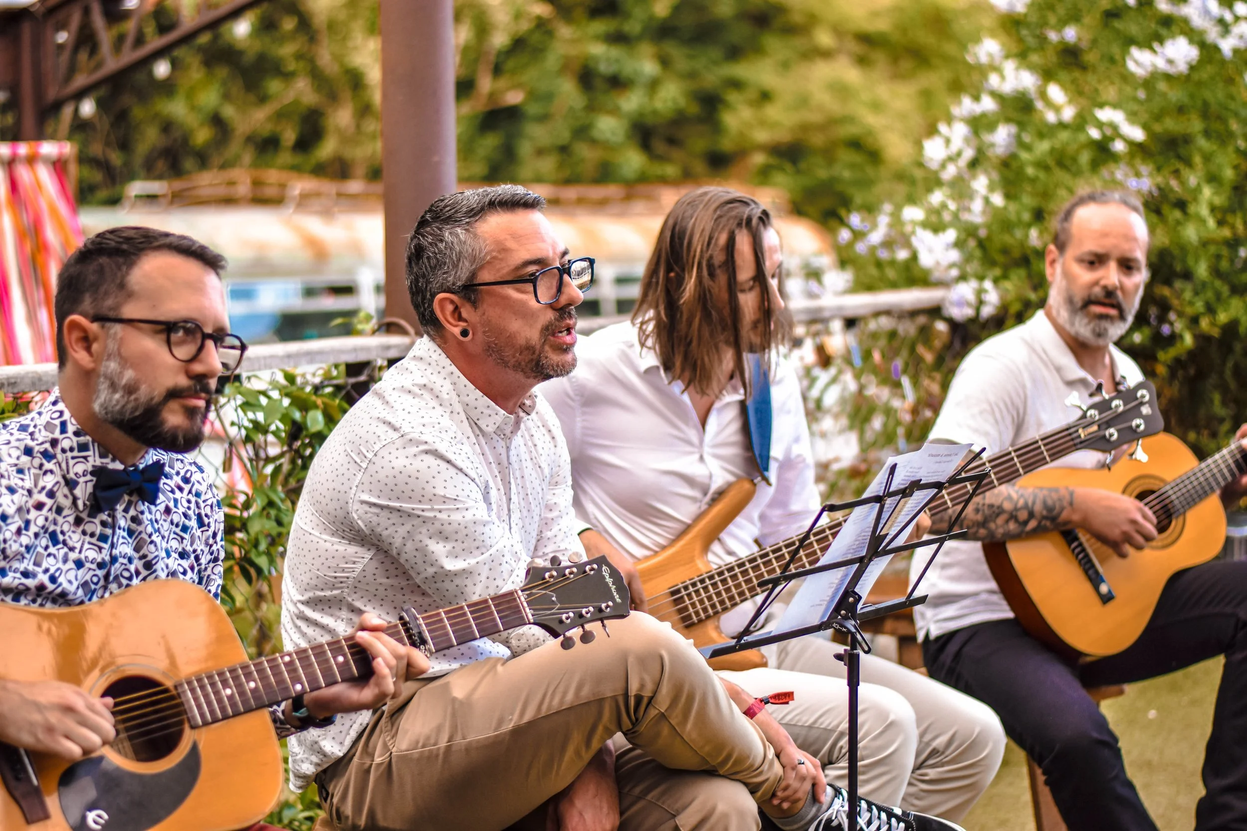 Un groupe de musiciens jouant de la guitare lors d'une performance en plein air, entouré d'arbres et de verdure.