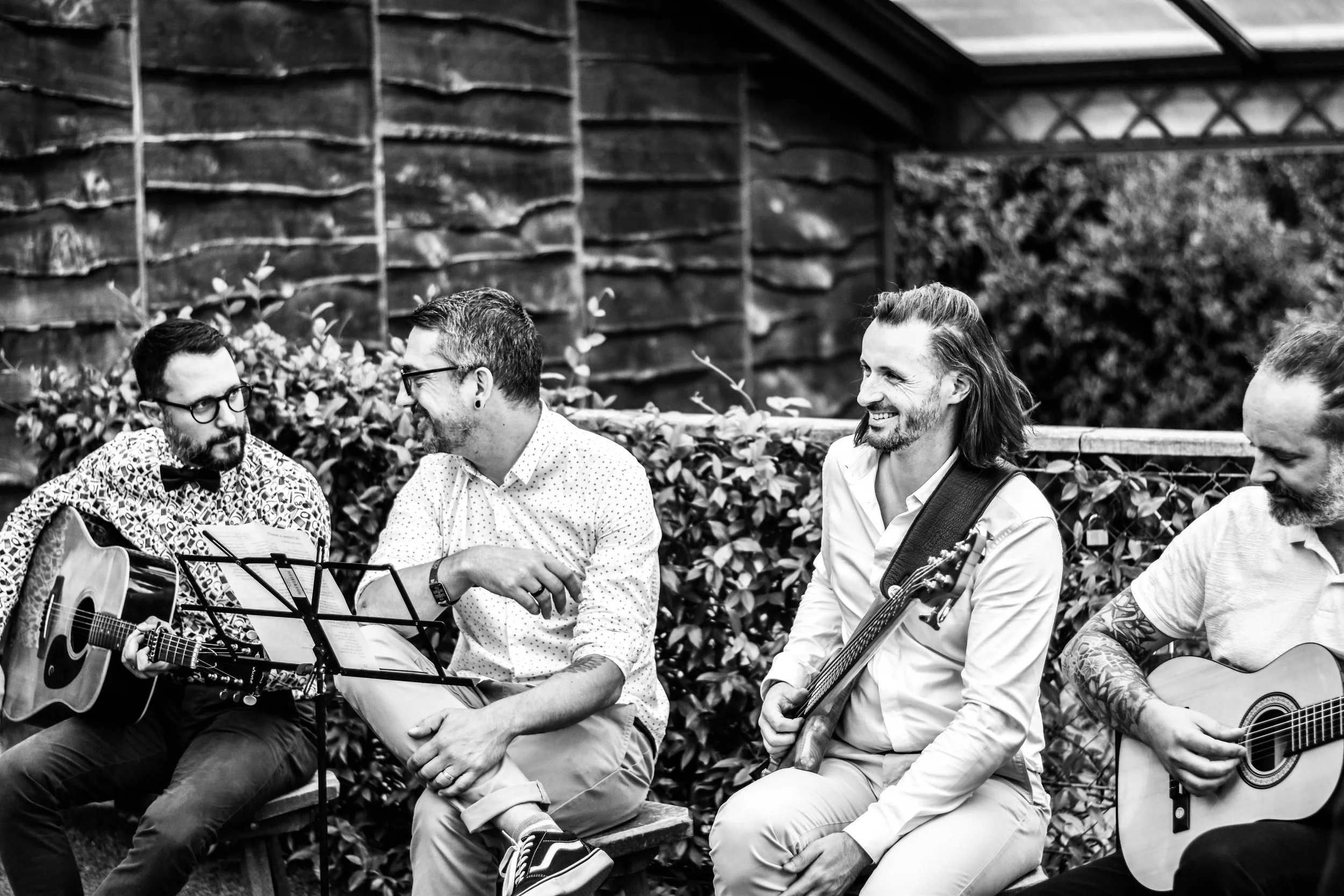 Groupe de musiciens assis sur un banc dehors, certains jouant de la guitare, lors d'une séance de musique en plein air.