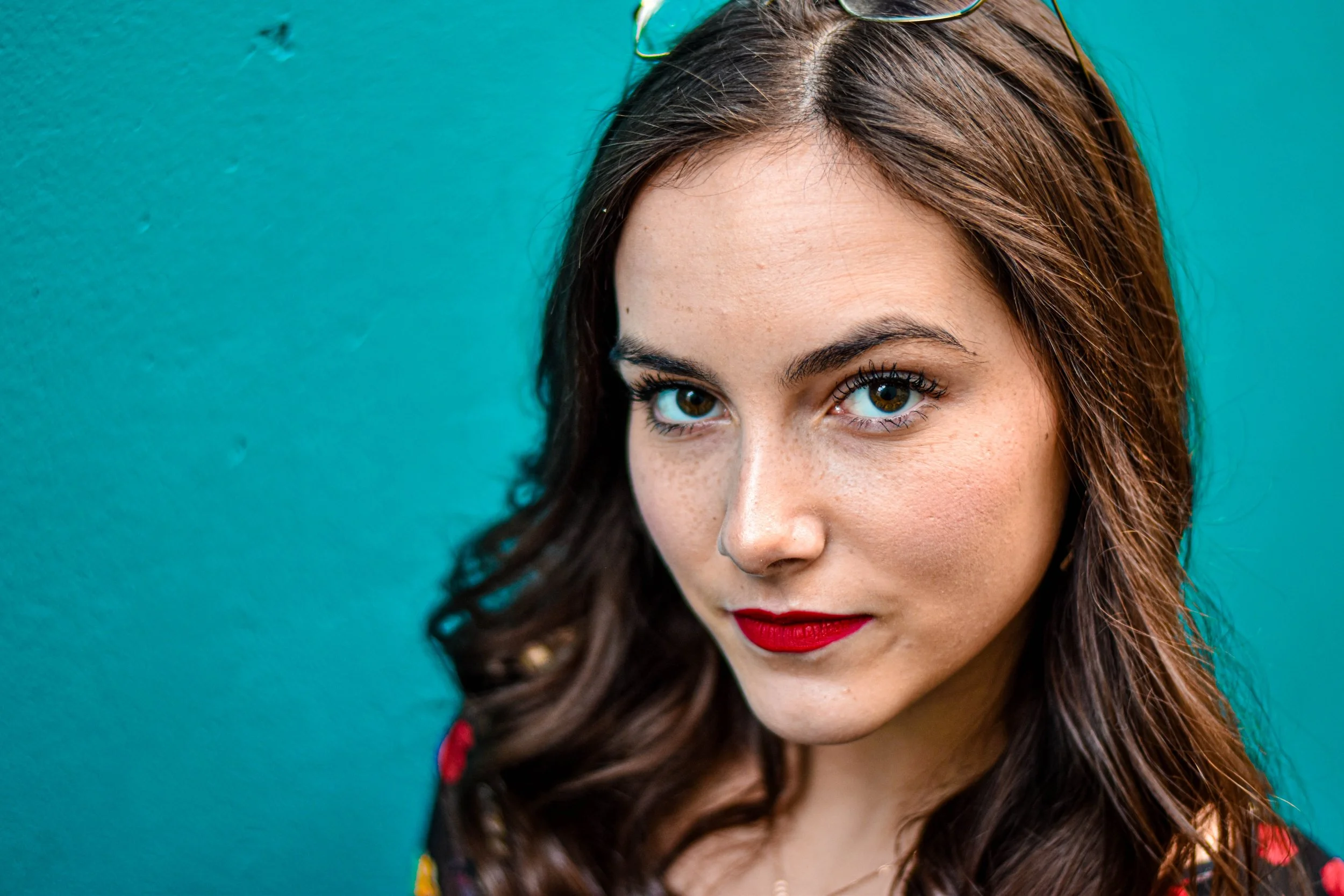 Portrait d'une femme avec cheveux bruns, yeux marrons et maquillage rouge, contre un mur turquoise.