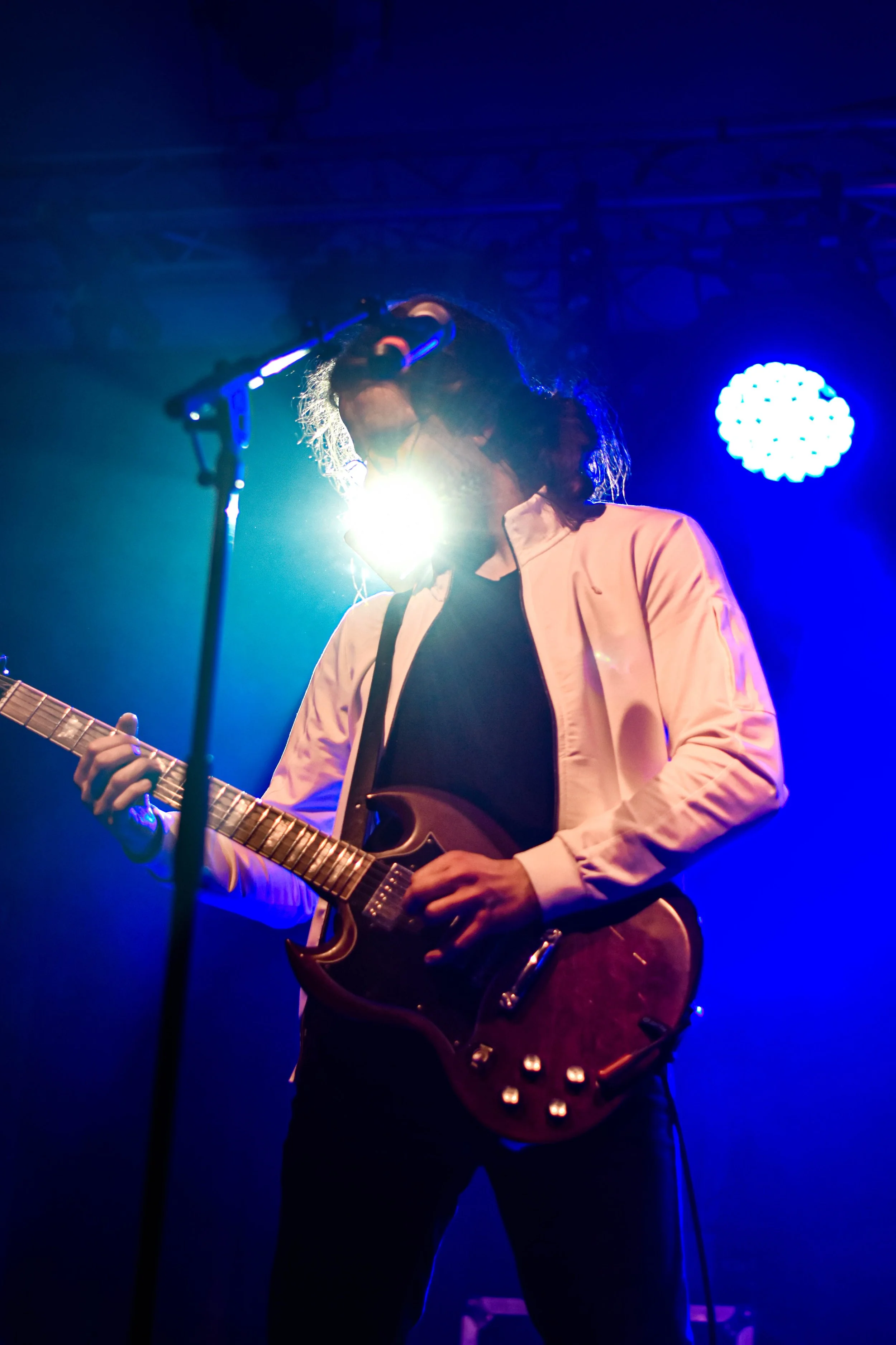 Musicien jouant de la guitare électrique sur scène sous un éclairage bleu et violet.