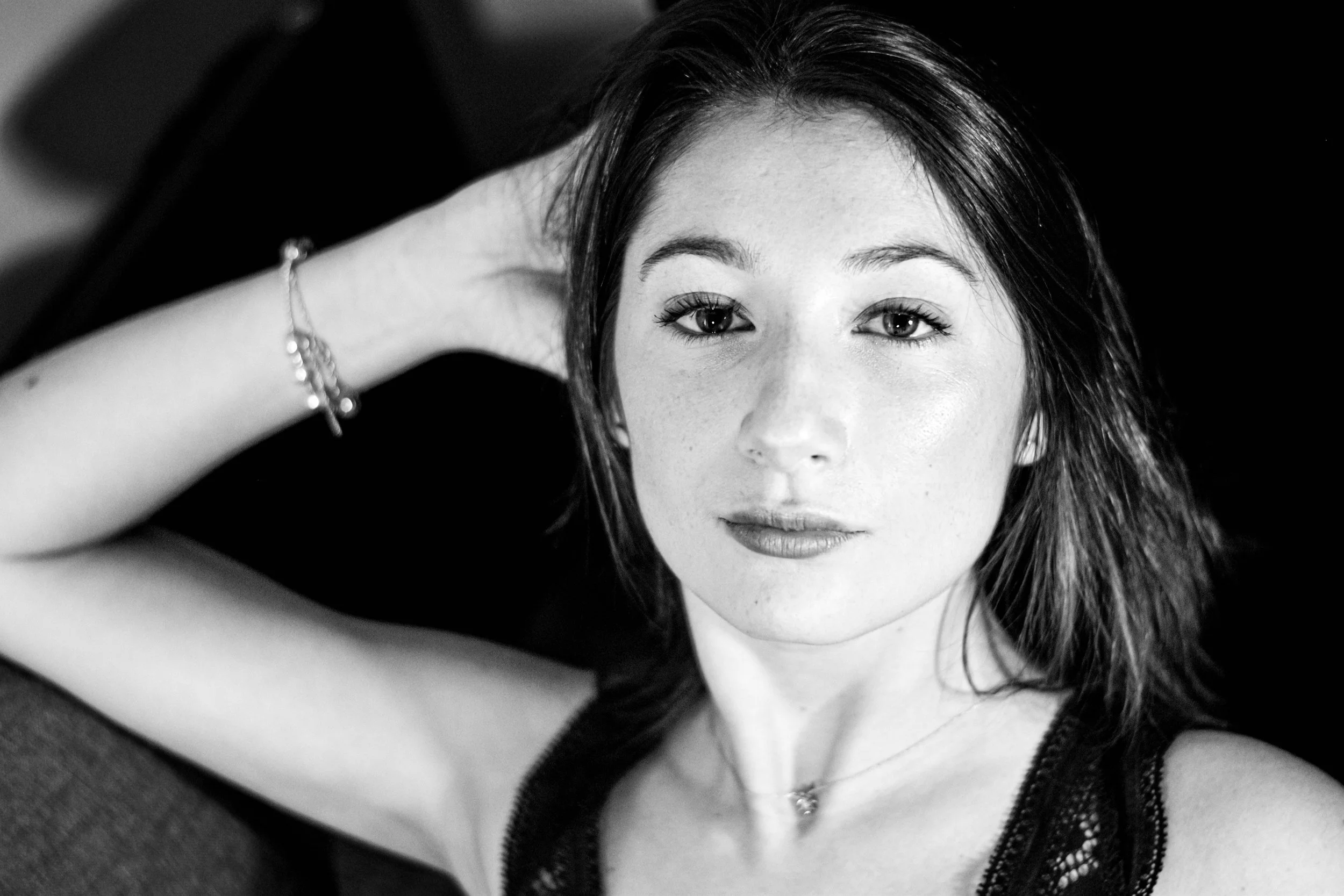 une jeune femme aux cheveux longs et noirs, visage clair, portant un bracelet et une chaîne, regardant fixement l'appareil photo, en noir et blanc.