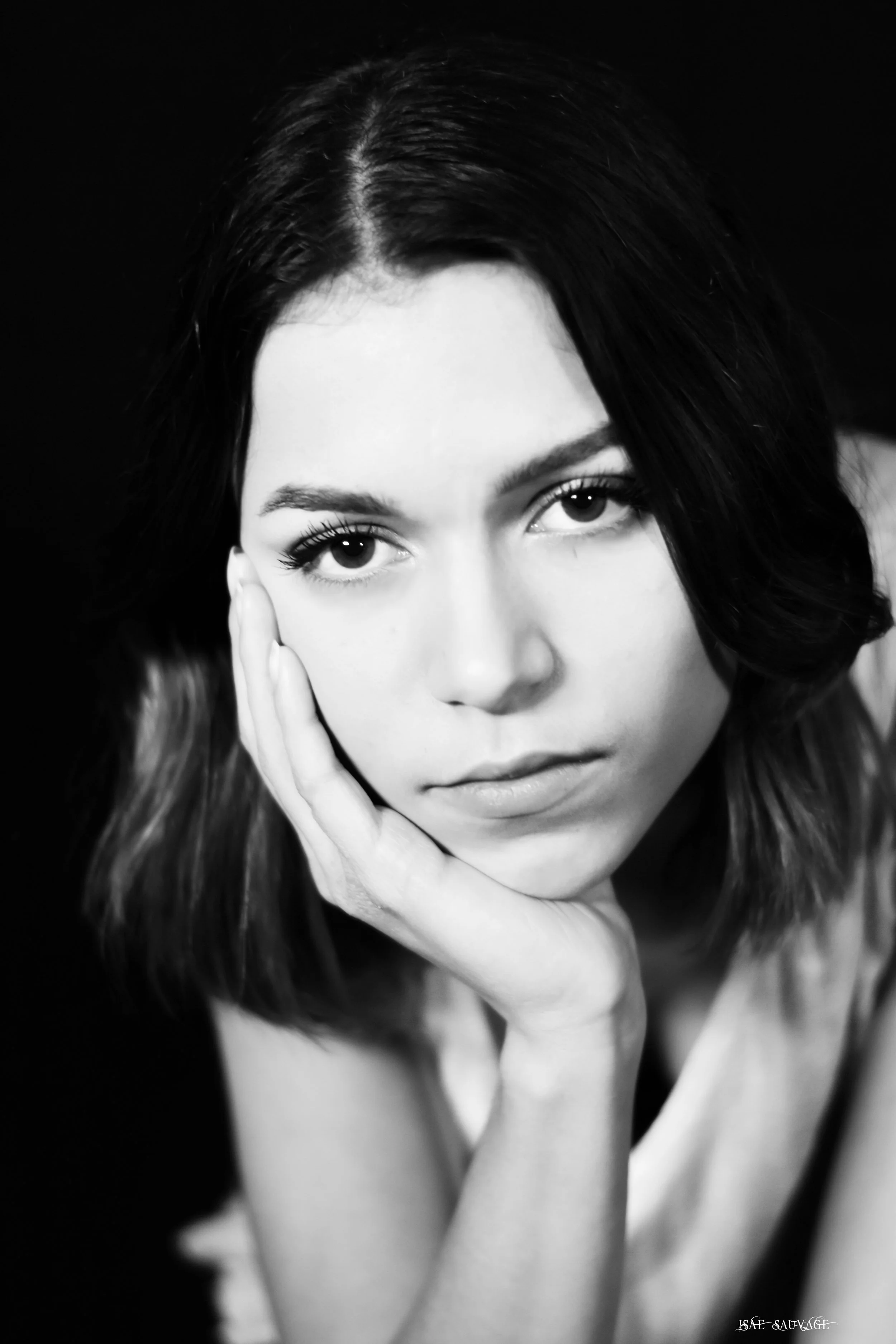 Portrait en noir et blanc d'une femme aux cheveux ondulés, regardant vers l'avant, tenant son visage avec une main. Signature en bas à droite.