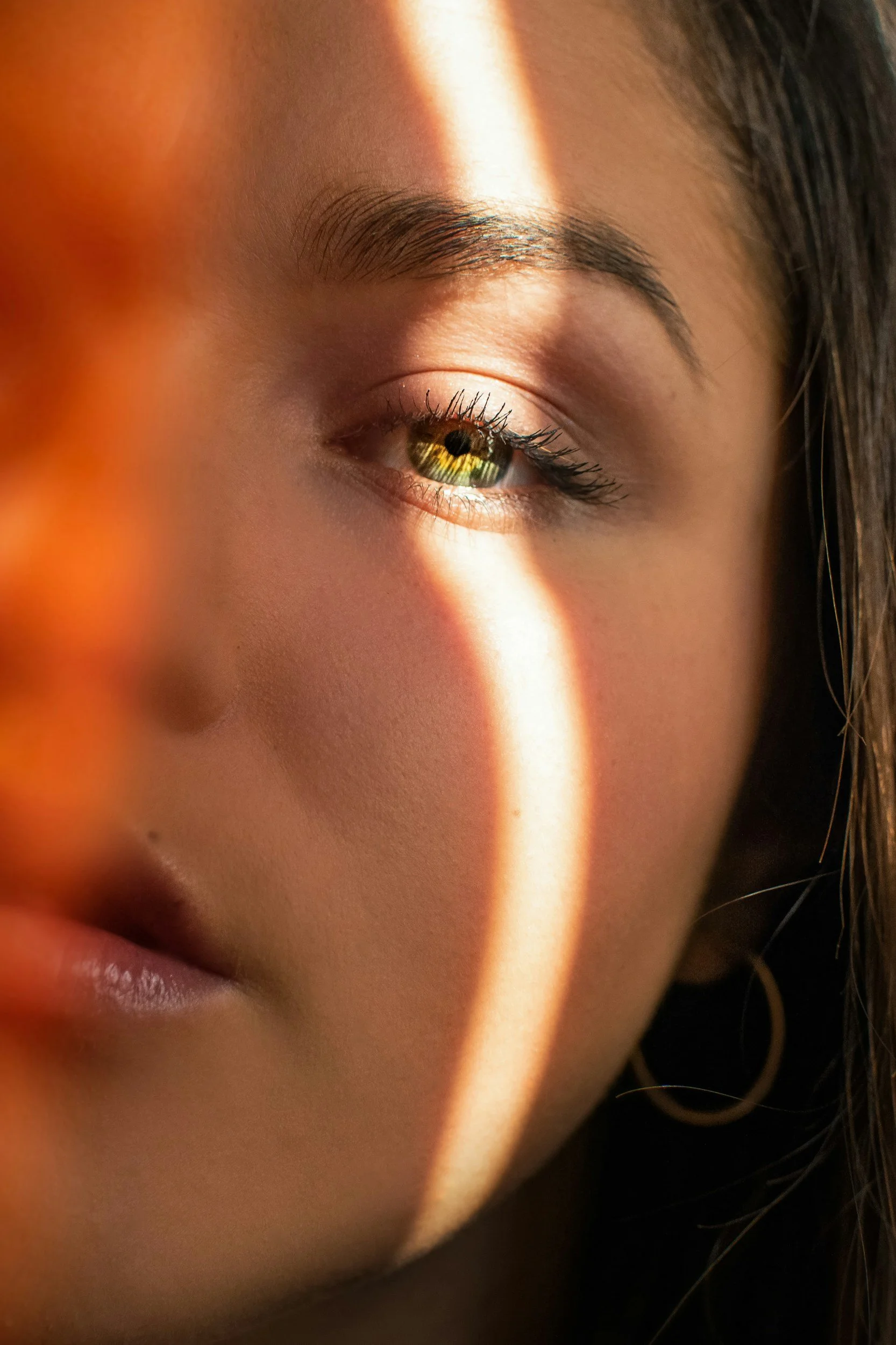Close-up of a woman's face with sunlight creating a streak of light across her eye and cheek, highlighting her eye details and skin texture.