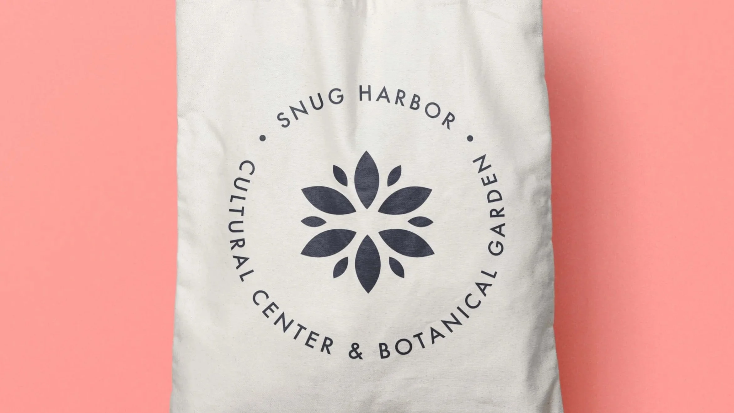 Various branded items including a tote bag, business cards, a stamp, and a smartphone displaying the company's logo and contact information, all featuring the logo for Snug Harbor Cultural Center & Botanical Garden.