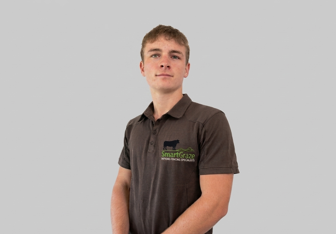 Young man wearing a brown polo shirt with a logo for SmartGraze and a cow graphic, standing against a light gray background.