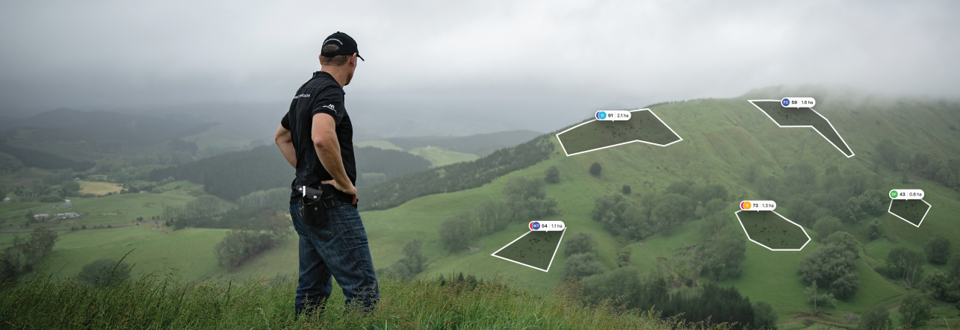 A man in a black shirt and jeans overlooking a lush green hillside with several overlaid golf course hole layouts and distances.