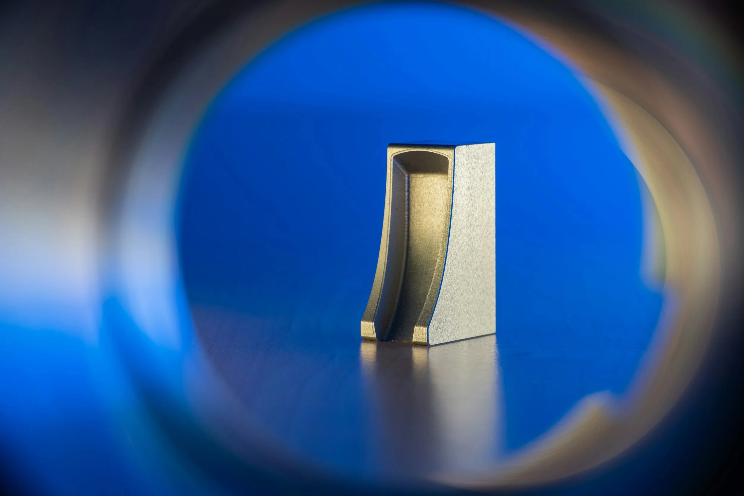 A metallic object viewed through a circular opening with a blue background.