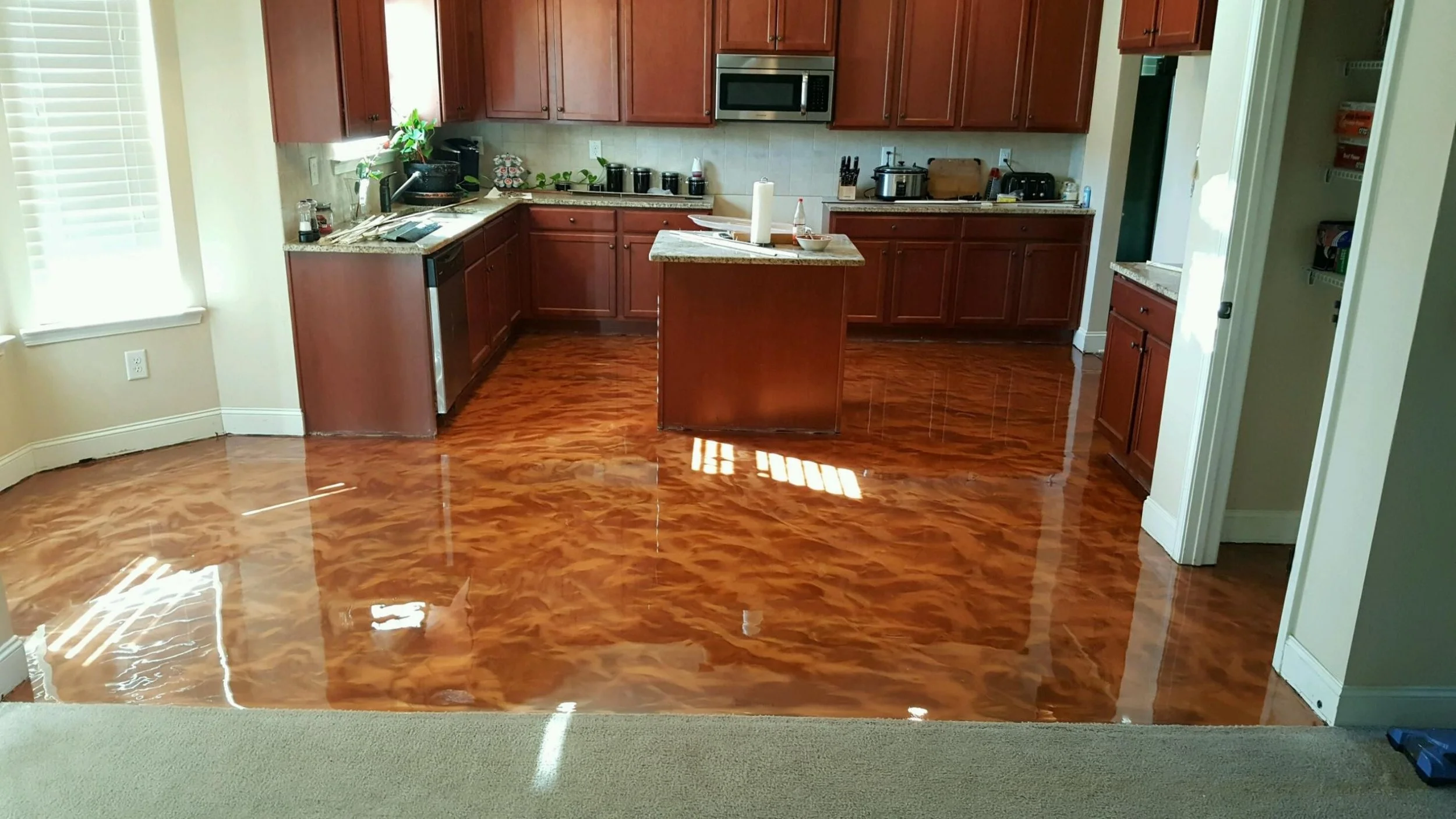 Kitchen with shiny, polished epoxy floor, wooden cabinets, stainless steel appliances, and a small kitchen island in the center.
