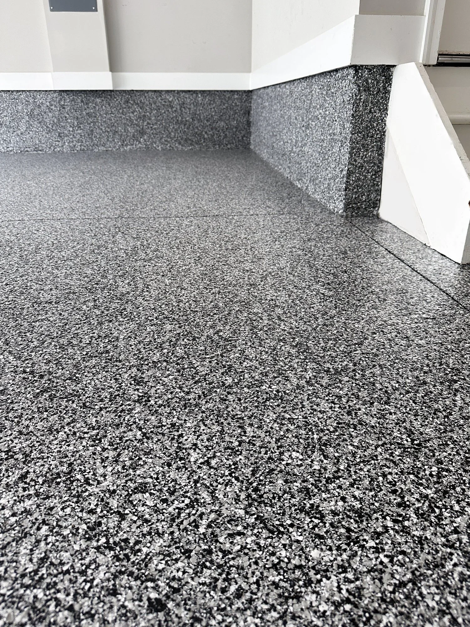 Close-up view of a speckled grey and black textured floor and step, with part of a white wall and baseboard visible.